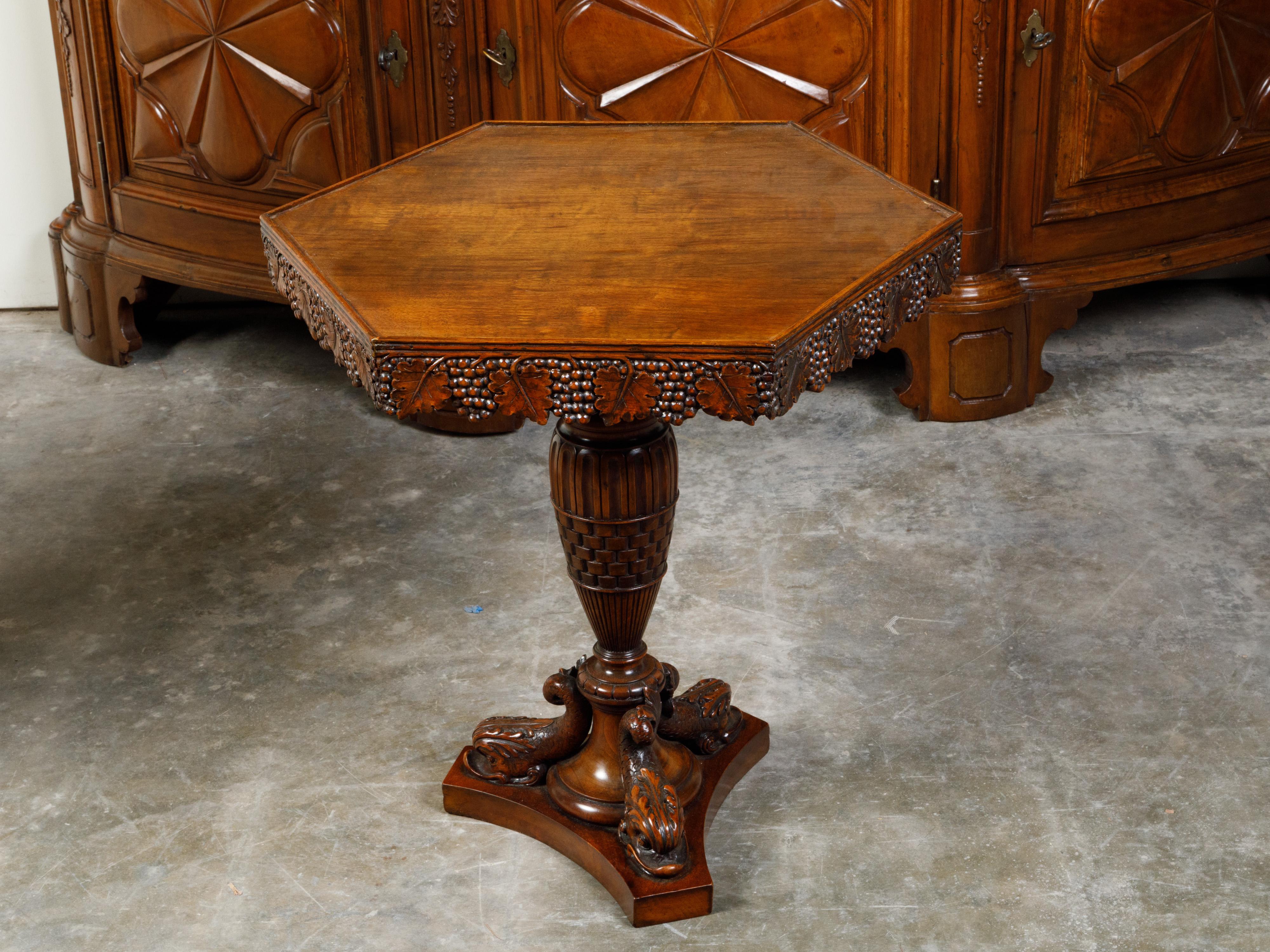 An English walnut side table from the 19th century, with hexagonal top, grape vine carved apron and dolphin motifs. Created in England during the 19th century, this walnut side table features an hexagonal top beautifully adorned with grapes and vine