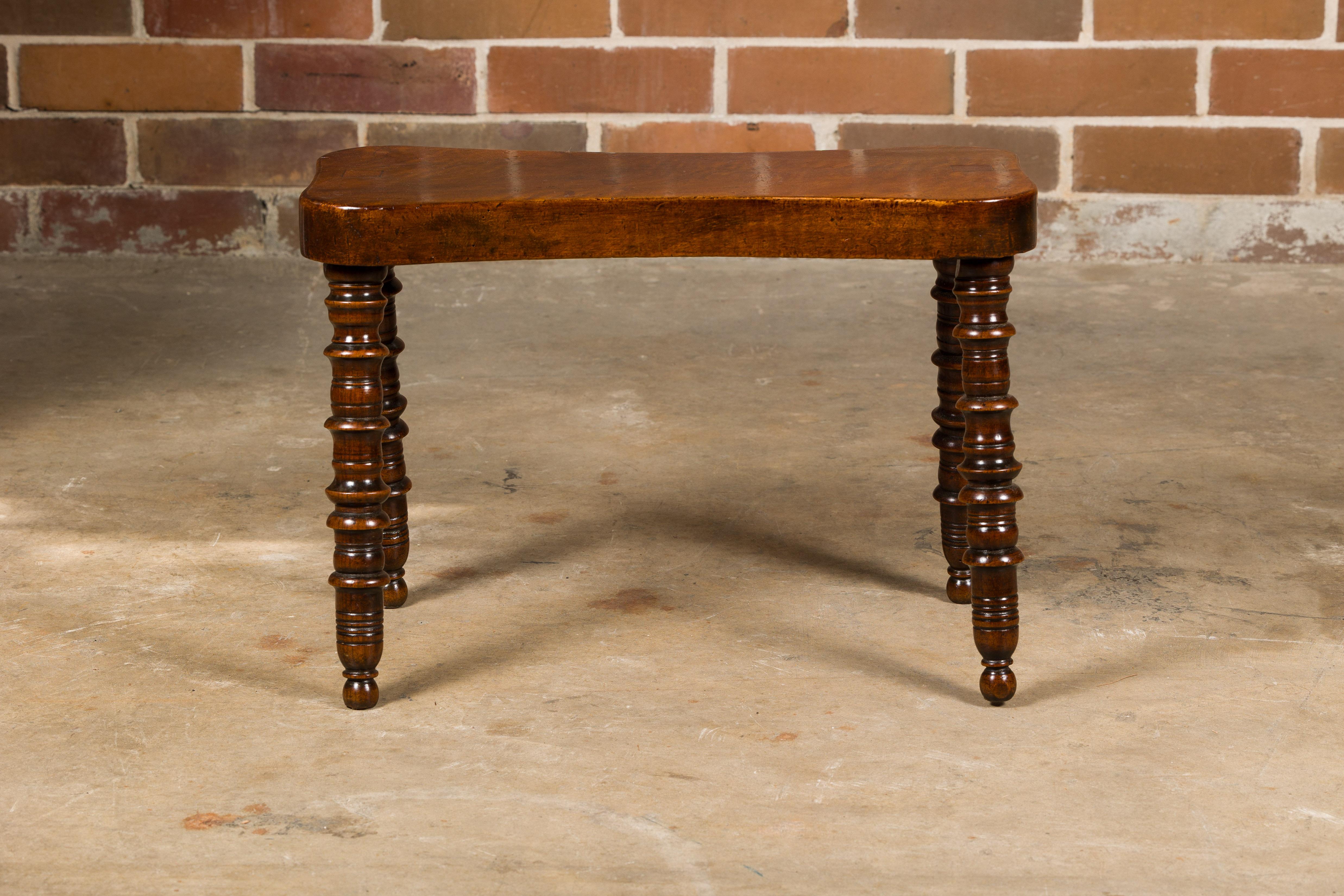 An English walnut stool from the 19th century with turned legs, petite ball feet and curving seat. Discover the timeless charm of this 19th-century English walnut stool, a piece that beautifully captures the essence of Victorian craftsmanship and