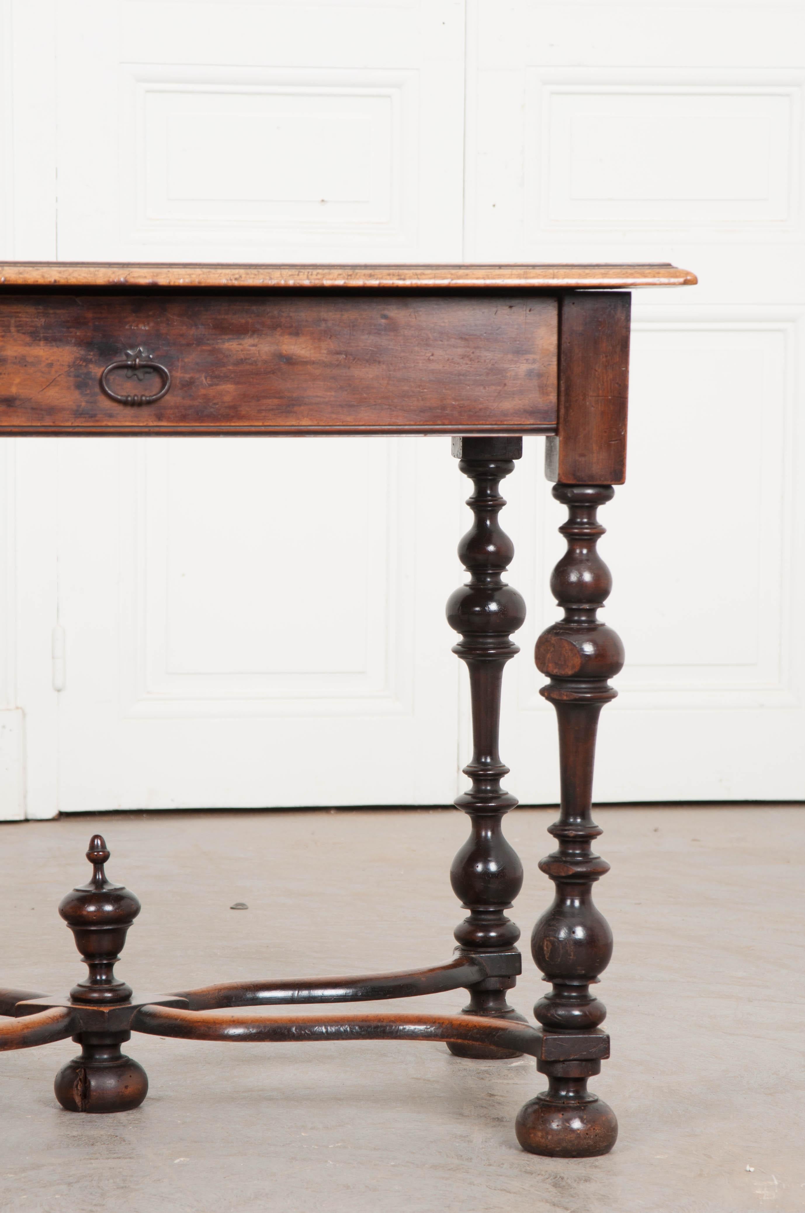 An extraordinary table in walnut, could serve multiple functions, such as an occasional table or a small writing desk. The walnut top rests upon a wooden apron which houses one large drawer over elaborate wood turned legs of the William and Mary