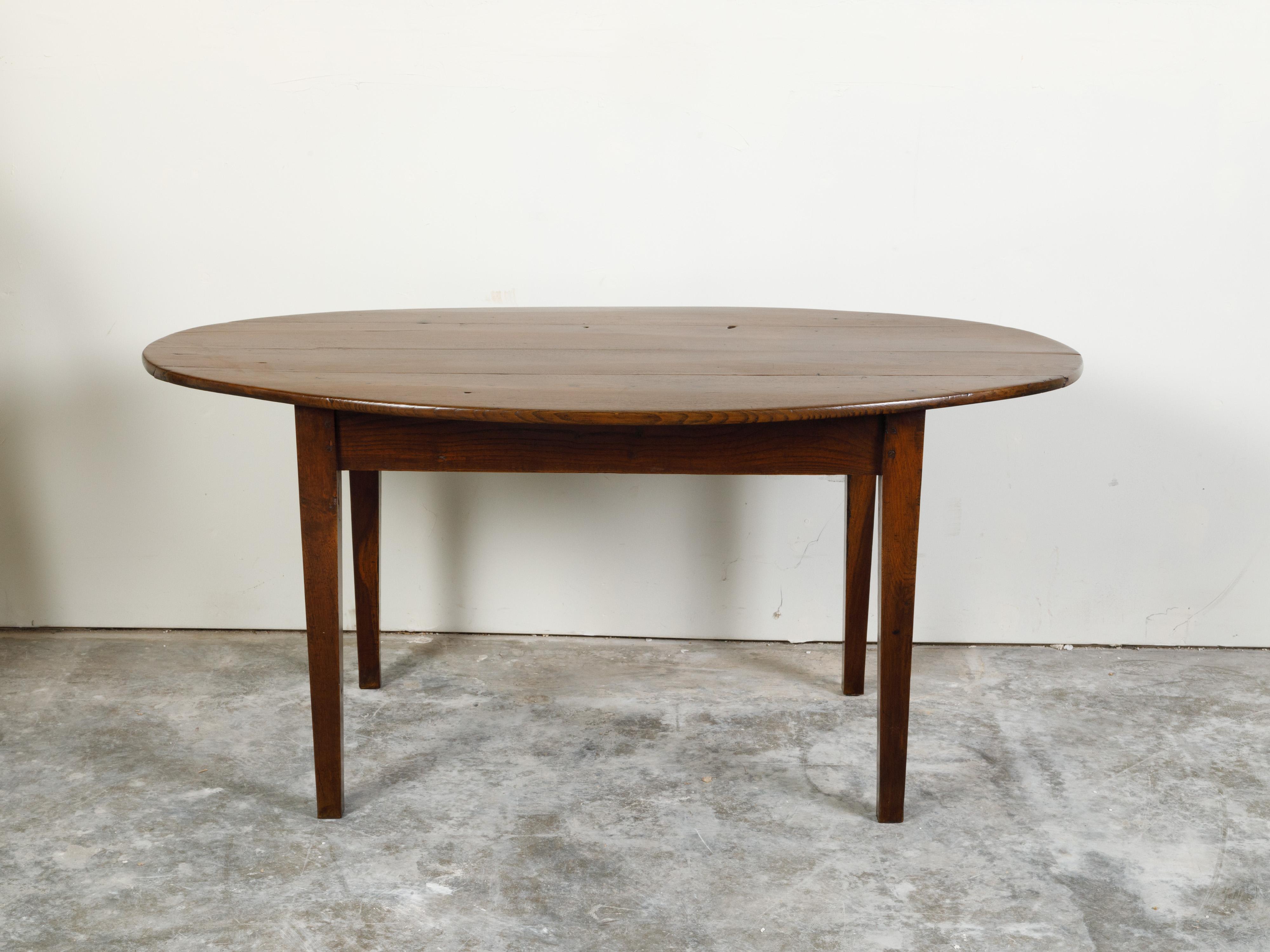 An English oval walnut table from the 19th century, with tapered legs. Created in England during the 19th century, this walnut table features an oval planked top sitting above a simple rectangular apron. Raised on four tapered legs and boasting a