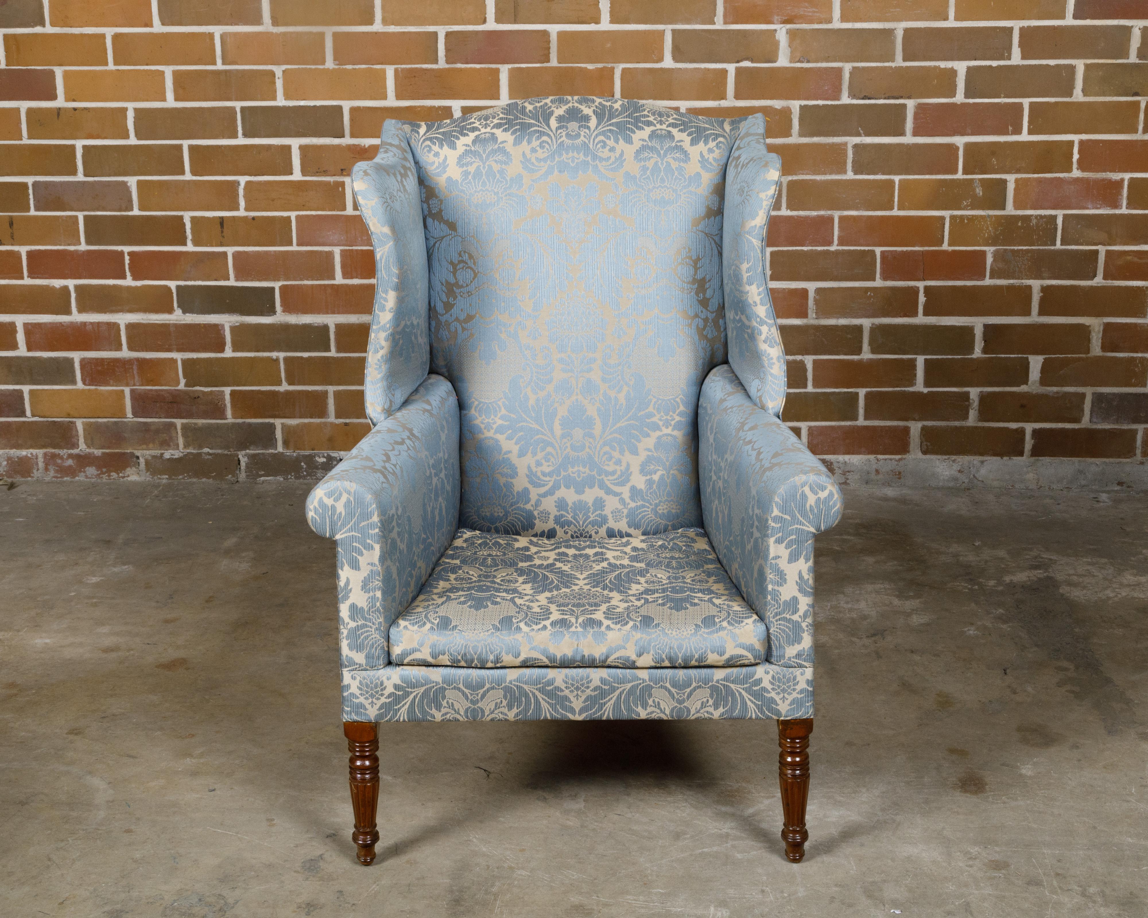An English wingback chair from the 19th century with blue fabric, turned legs in the front and saber ones in the back. This English wingback chair from the 19th century is upholstered in a rich blue fabric, offering a striking contrast to the dark
