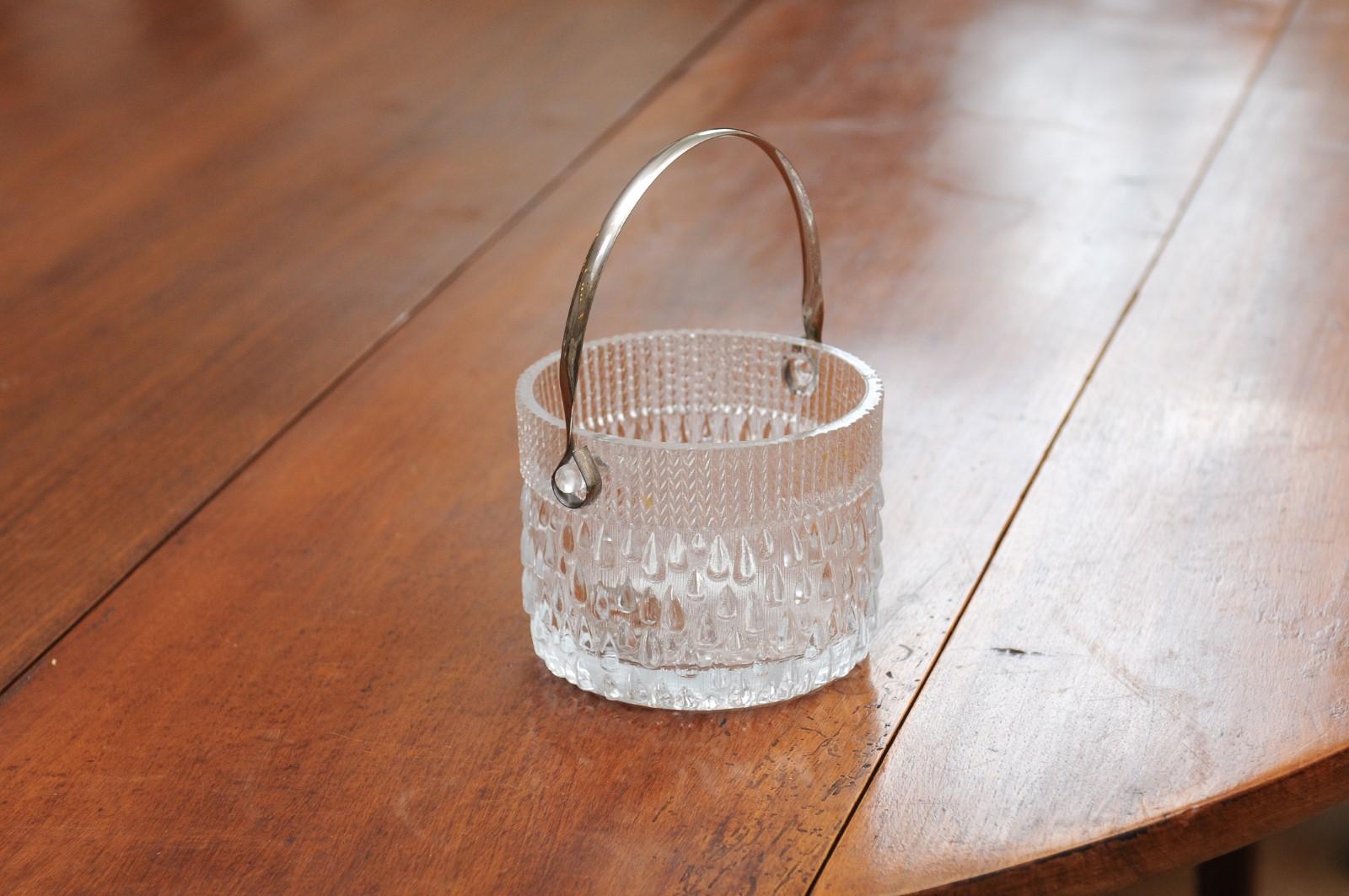 An English cut glass ice bucket from the 20th century, with silver spoon, large handle and teardrop motifs. Created in England during the 20th century, this cut glass ice bucket features a circular shape harmoniously accented with teardrop motifs.