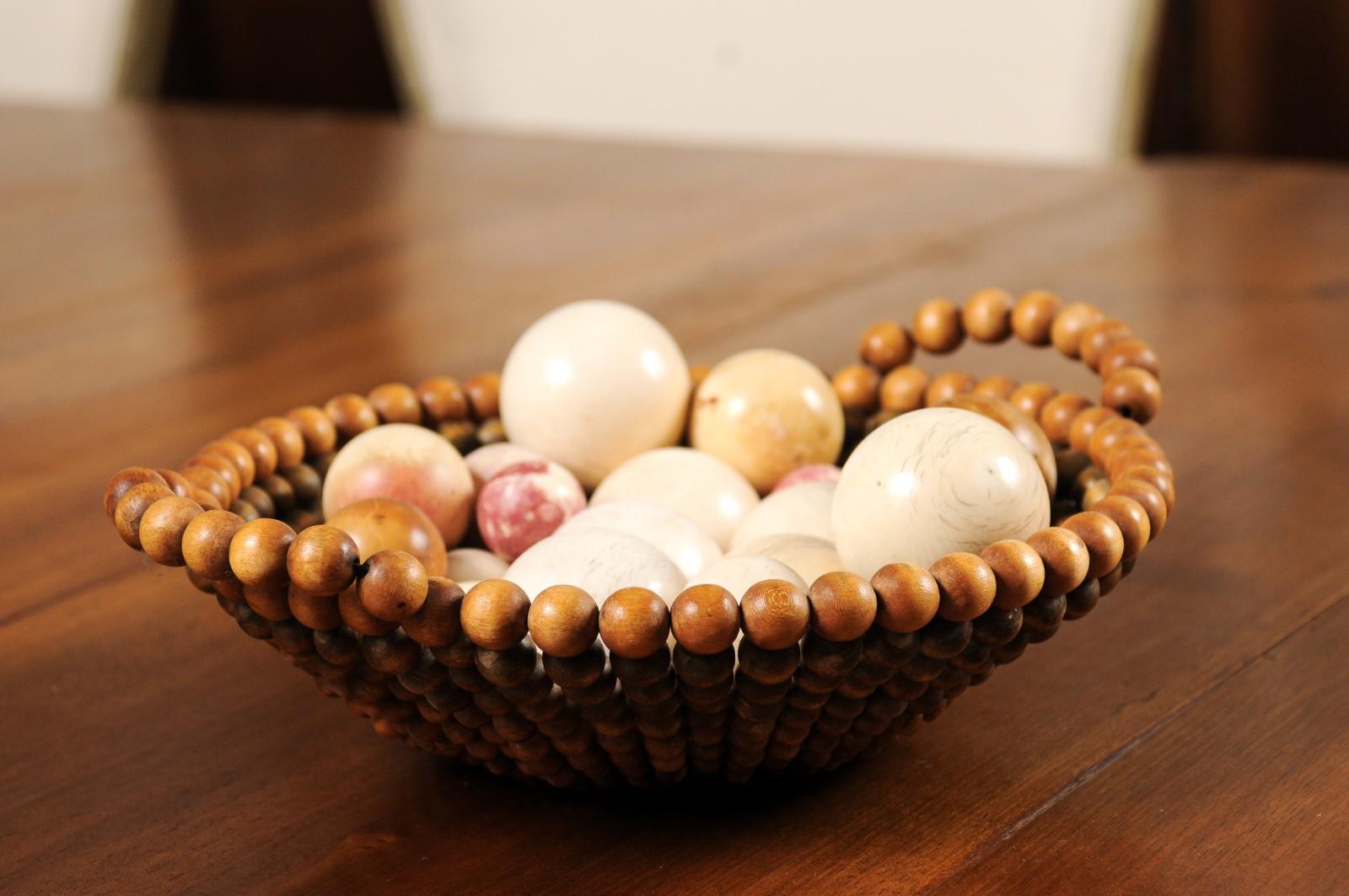 An English decorative wooden bead basket from the 20th century adorned with an assortment of balls. Created in England during the 20th century, this bead wooden basket showcases tapering lines and side handles. Decorated with an assortment of