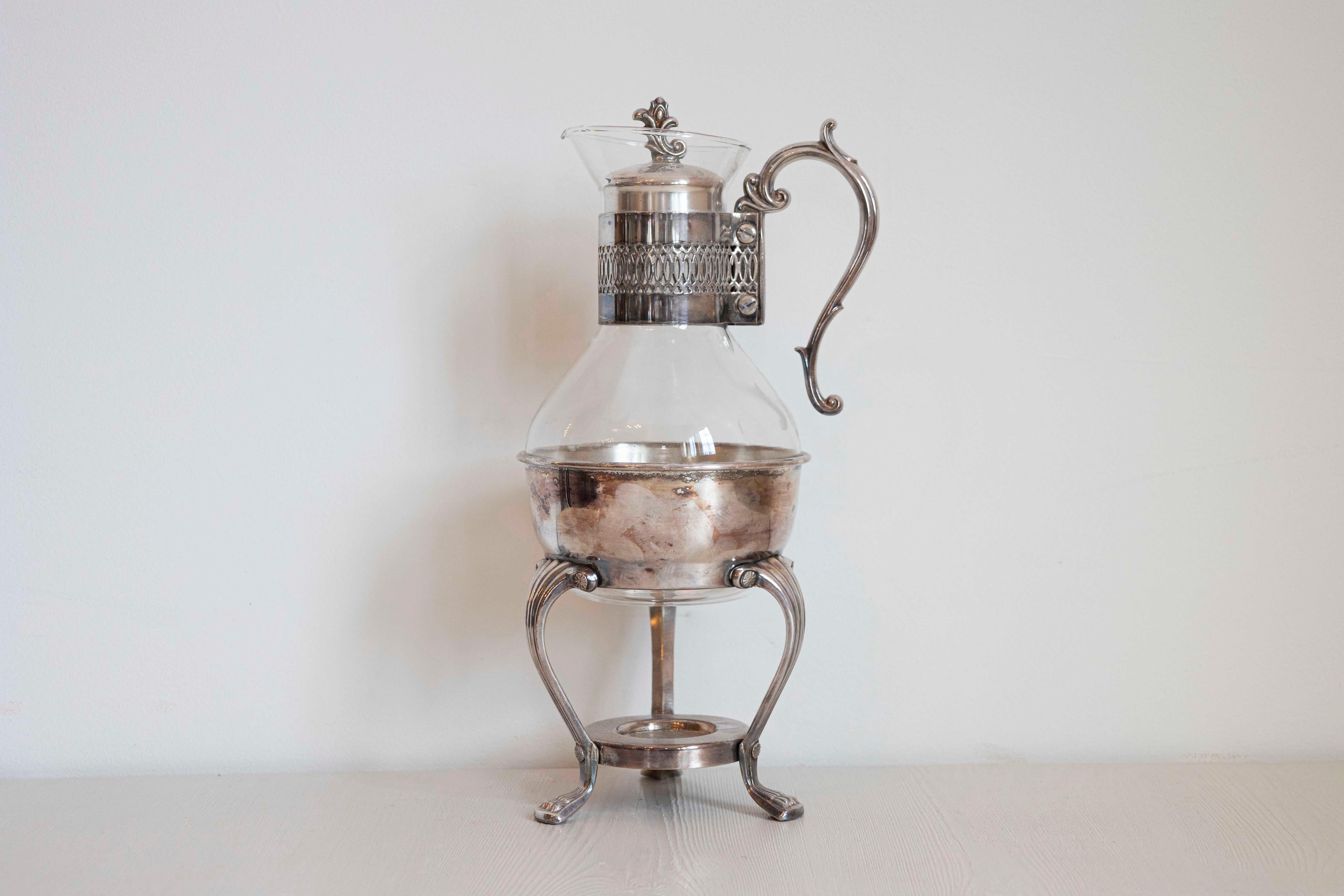 An English glass and silver coffee pitcher from the 20th century, with scrolling handle, pierced motifs and paw feet. Created in England during the 20th century, this pitcher features an elegant silhouette mixing glass and silver, accented with a