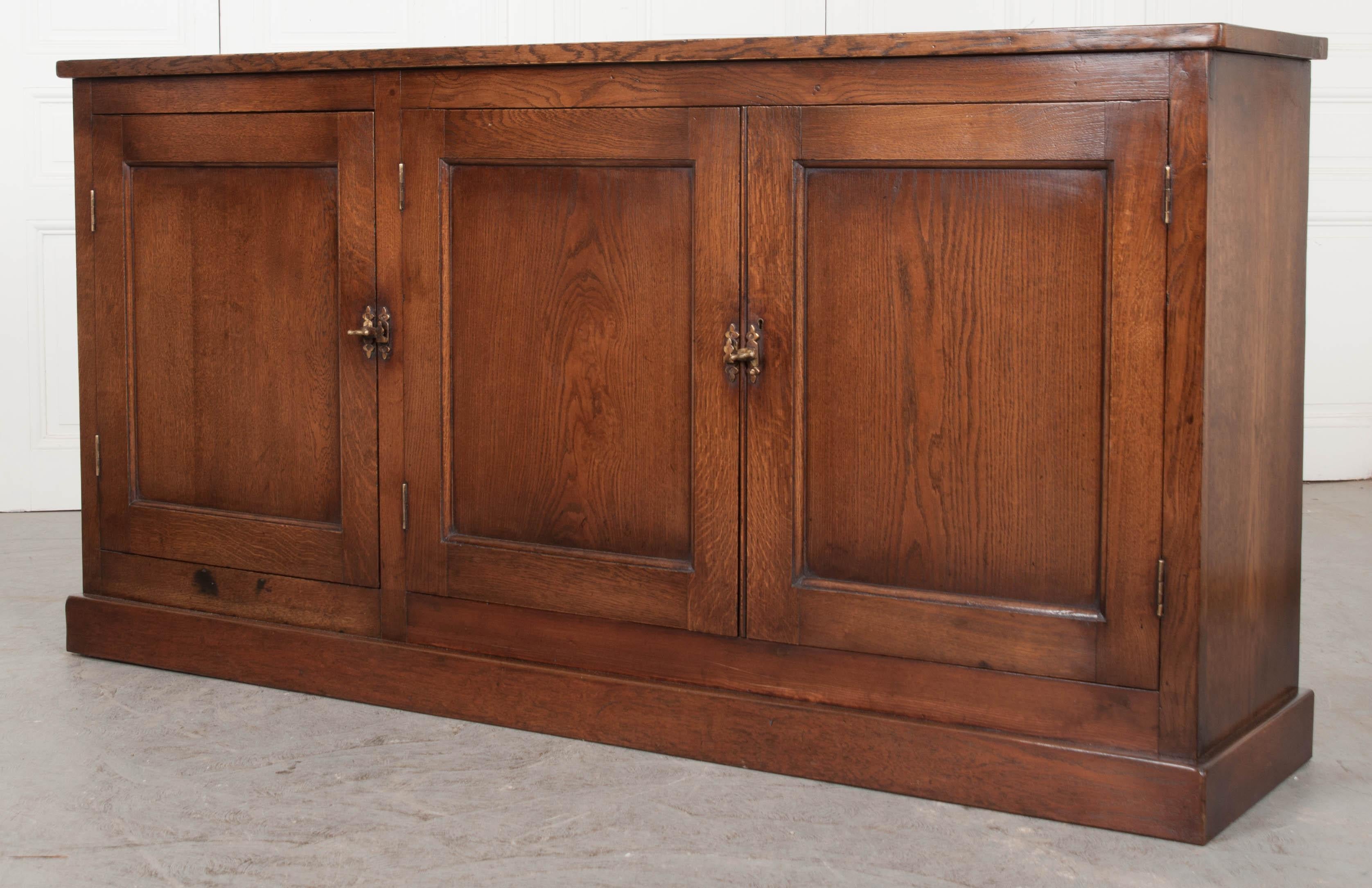 This fine English oak sideboard, circa 1900, offers plenty of storage yet its dimensions are perfect for smaller spaces. The three paneled doors, with brass latches and a single escutcheon (the key lacking) open to reveal a single removable shelf.