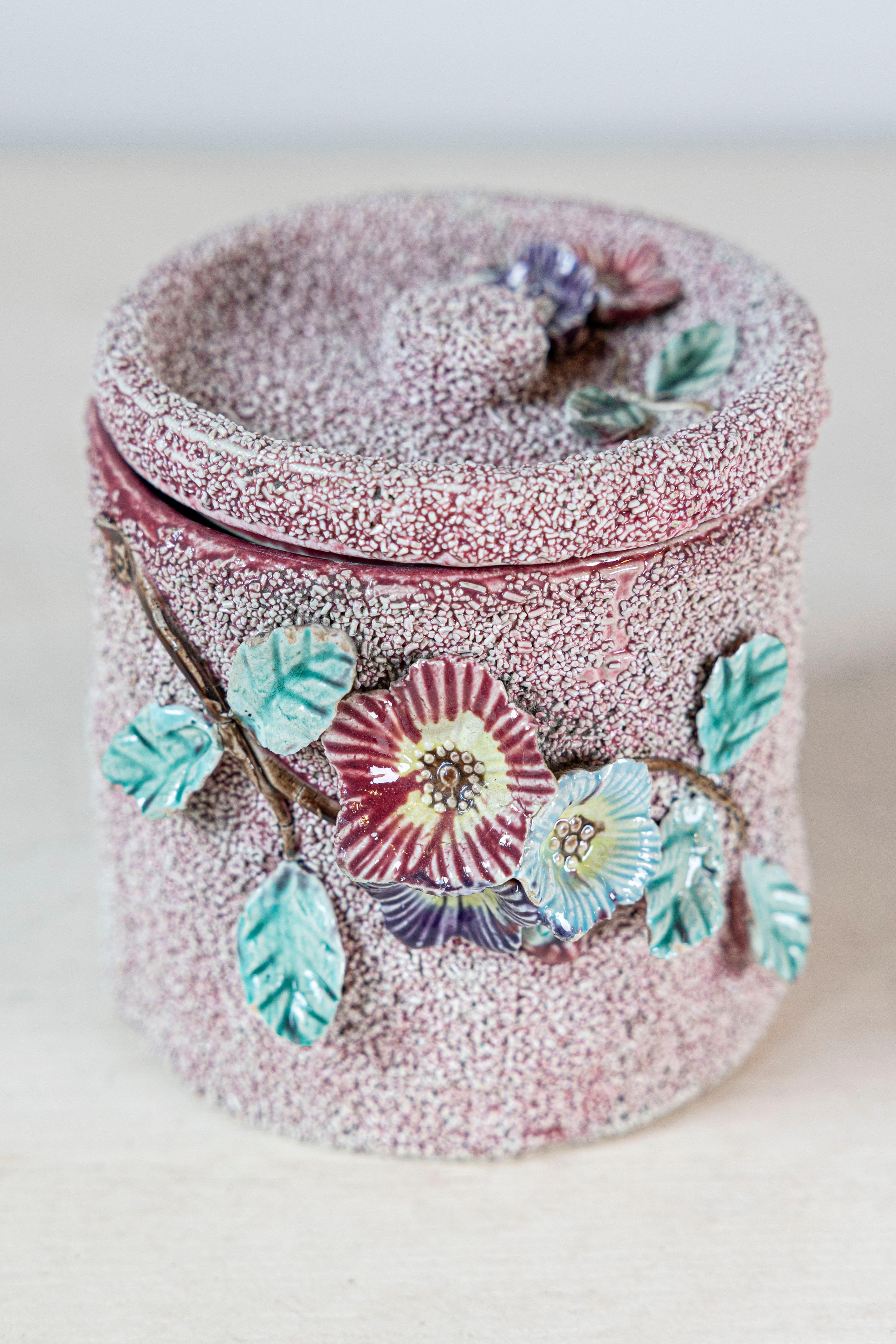 Caja de cerámica inglesa del siglo XX, con motivos florales, fondo texturado y tapa. Creado en Inglaterra durante el siglo XX, este recipiente decorativo presenta un cuerpo cilíndrico rematado con una tapa conformada. Adornada con flores rojas,