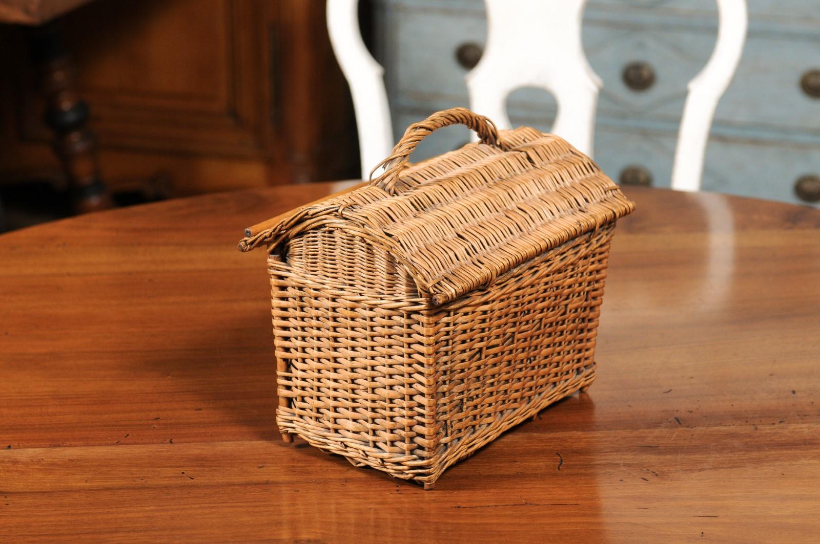 A rustic English wicker basket from the 20th century, with arching lift top and small handle. Created in England during the 20th century, this wicker basket features an arching roof-inspired lid opening thanks to a handle and a rod to reveal a small
