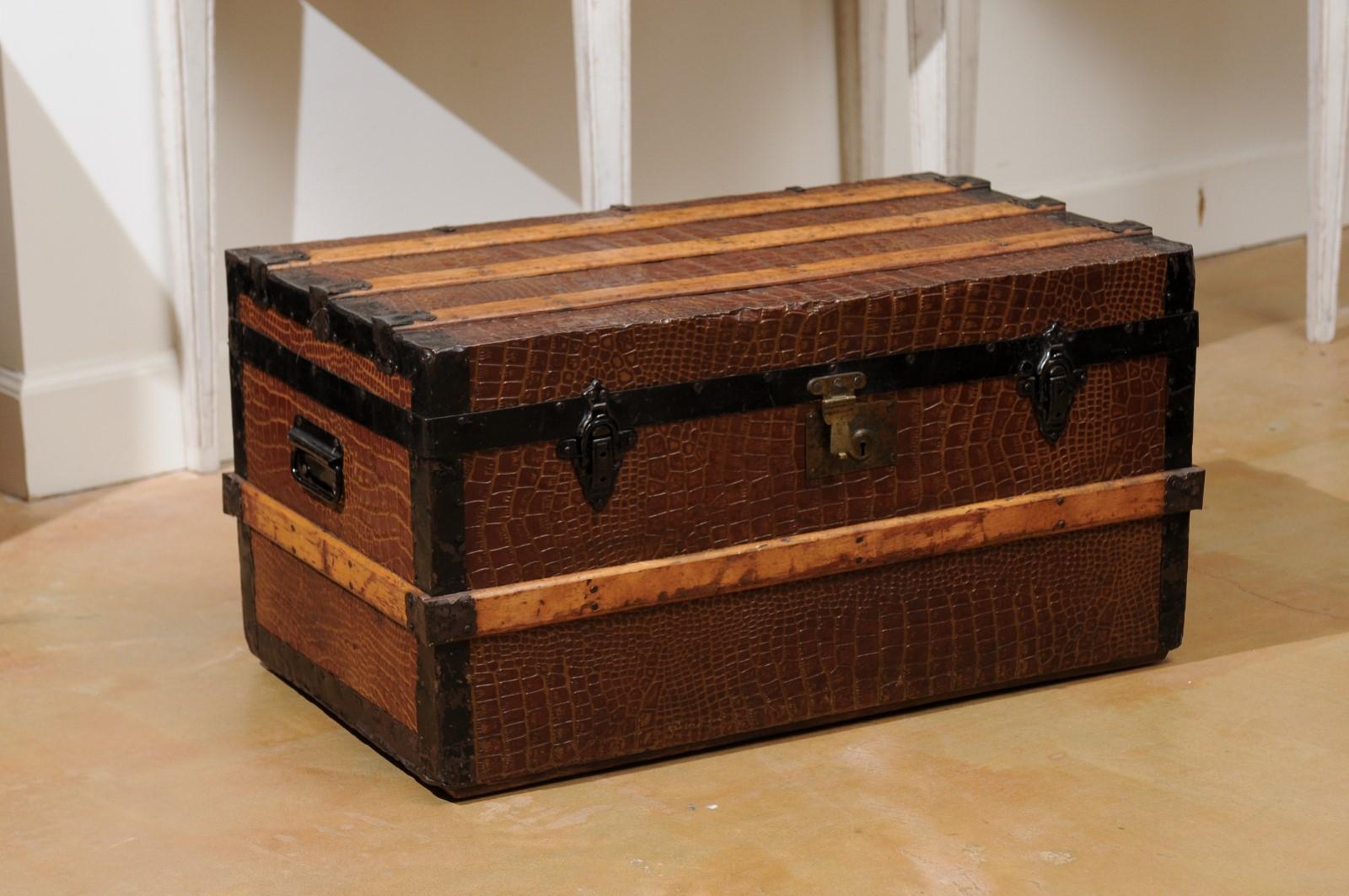 An English wood bound trunk from the 20th century, with iron details. Born in England during the 20th century, this handsome trunk features a linear silhouette perfectly accented by a textured surface and iron details. The hinged lid opens to reveal