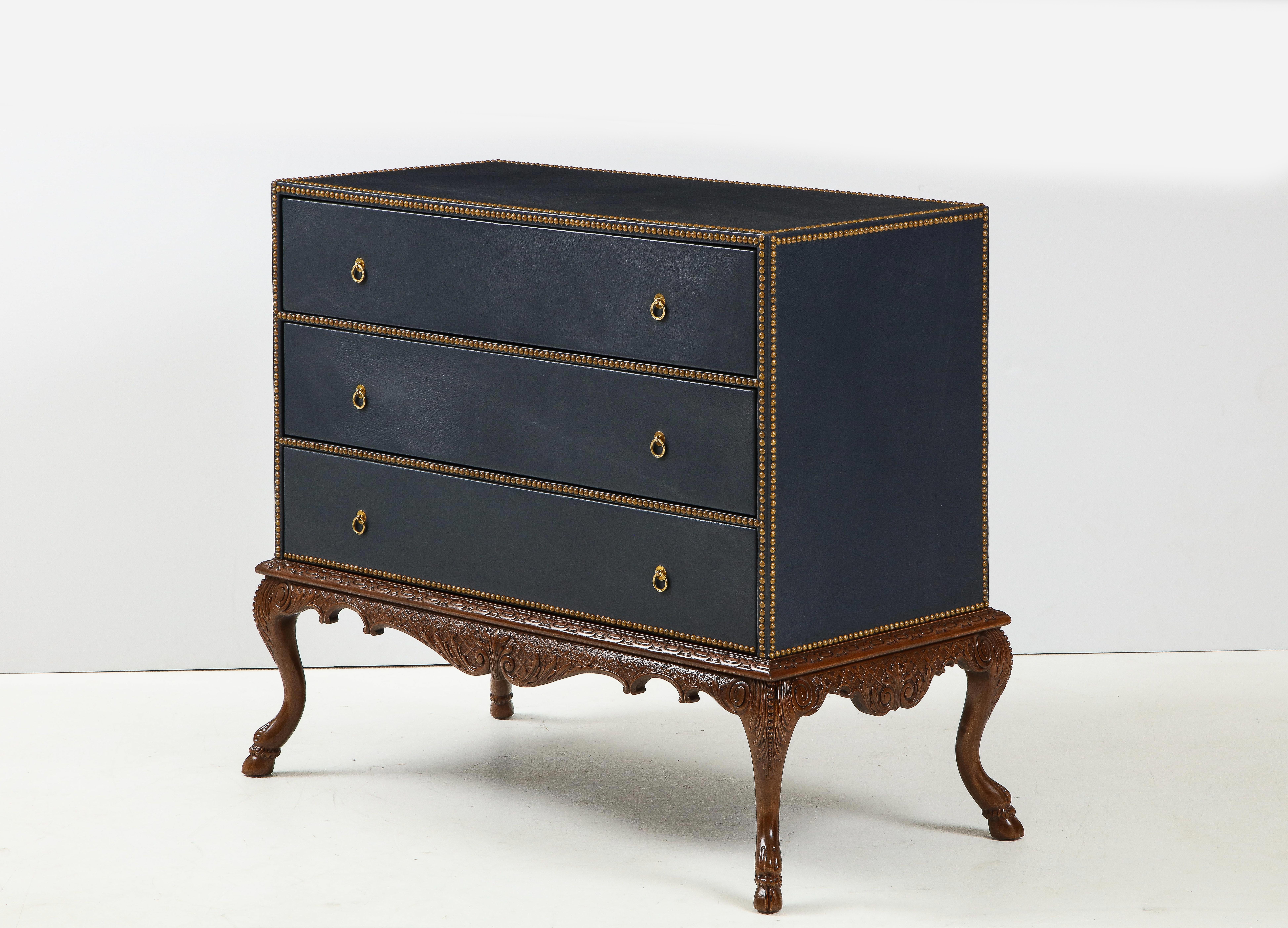Bespoke three drawer chest covered in petrol blue leather with hand hammered brass nailheads. Chest rests on hand carved stand with cloven feet and intricate front and side aprons, the 3 deep drawers provide ample storage. Covered back allows piece