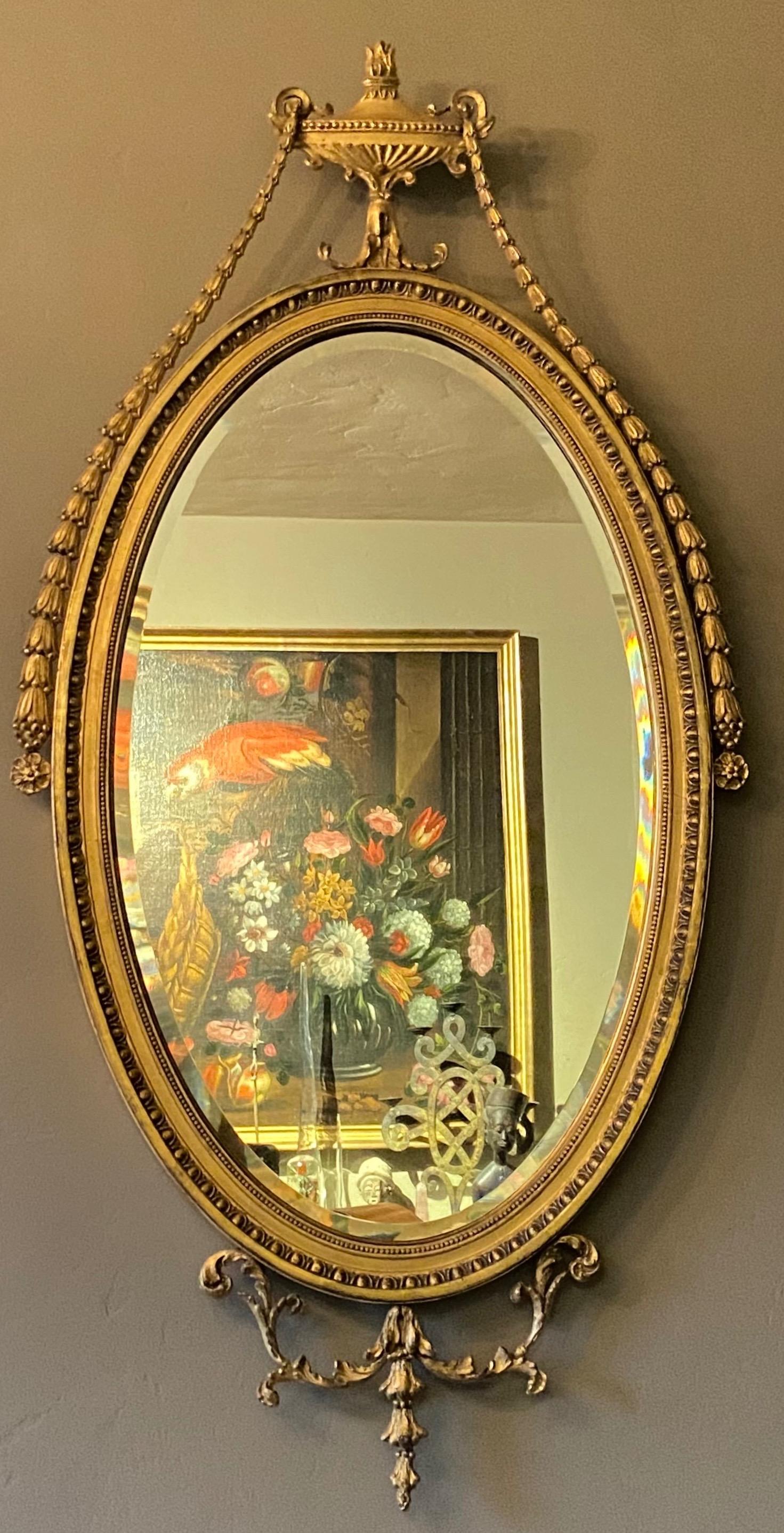 English Adam style gilt wood wall mirror with carved and cast oval frame, having an urn decoration at the top pediment with garland swags and flower spray.
High quality in excellent condition.
1st quarter 20th century.
We have another matching