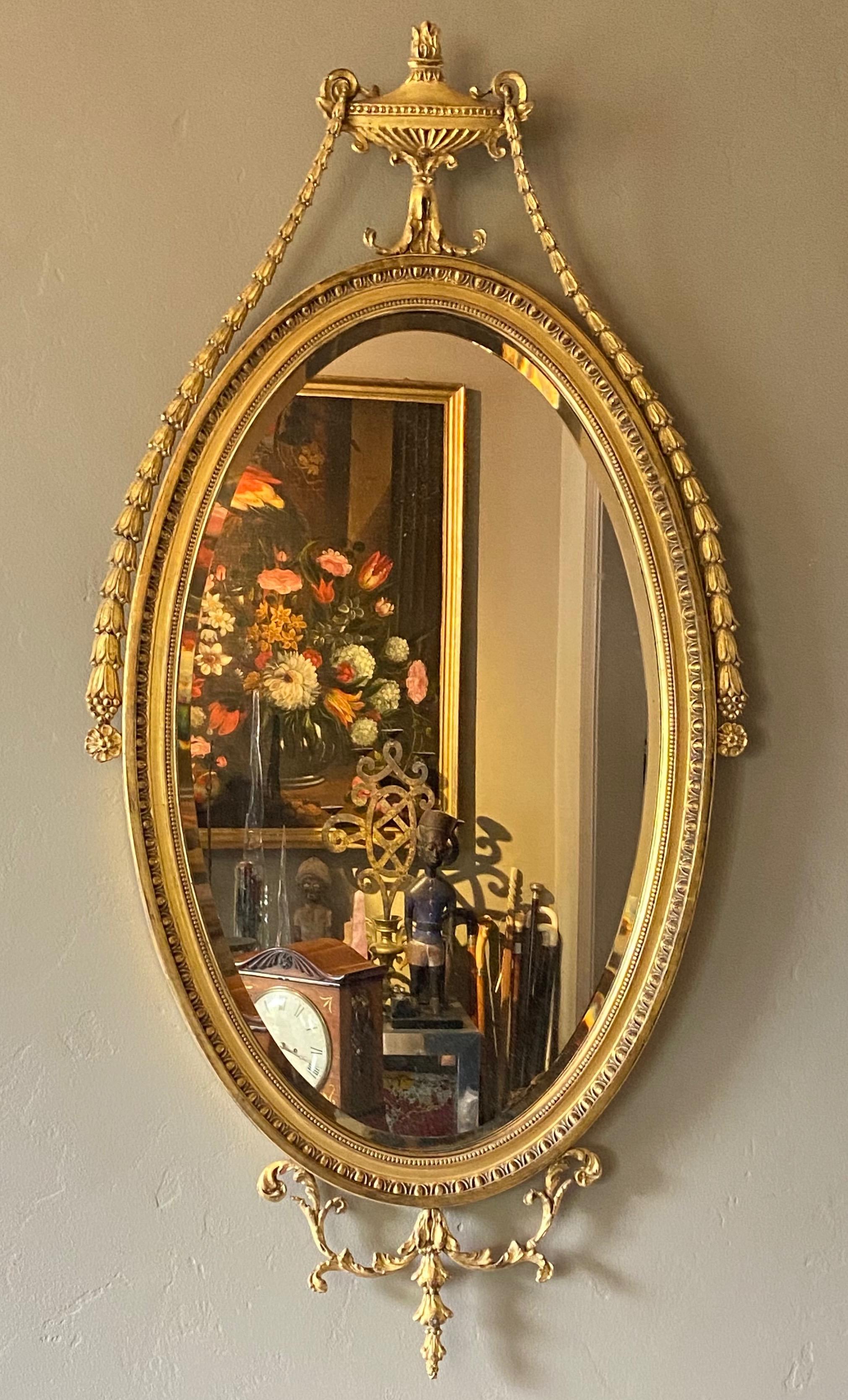 English Adam style gilt wood wall mirror with carved and cast oval frame, having an urn decoration at the top pediment with garland swags and flower spray.
High quality in excellent condition.
1st quarter 20th century.
We have a matching mate to