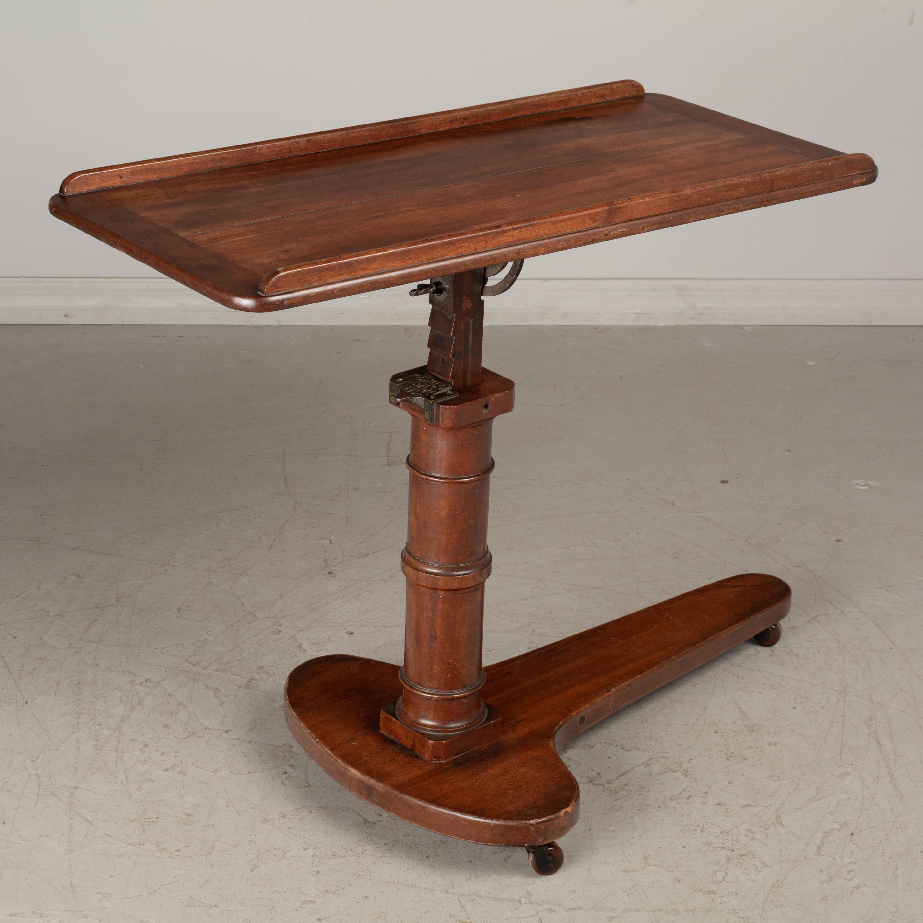 An early 20th century English mahogany adjustable tilt-top tray table, with cast iron mechanism. Tabletop may be tilted flat or angled and has a ledge on each side. Iron latch stamped: Carter's at London. The height adjusts from 21” to 42”. Base has