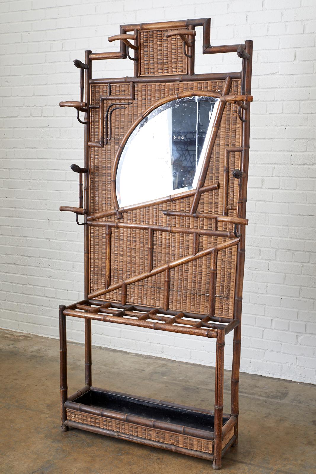 19th century bamboo hall tree and coat rack with umbrella stand made in the English aesthetic movement period. Features a stylized Asian fan motif beveled mirror surrounded by hat and coat hooks. The decorative frame is covered with a wicker