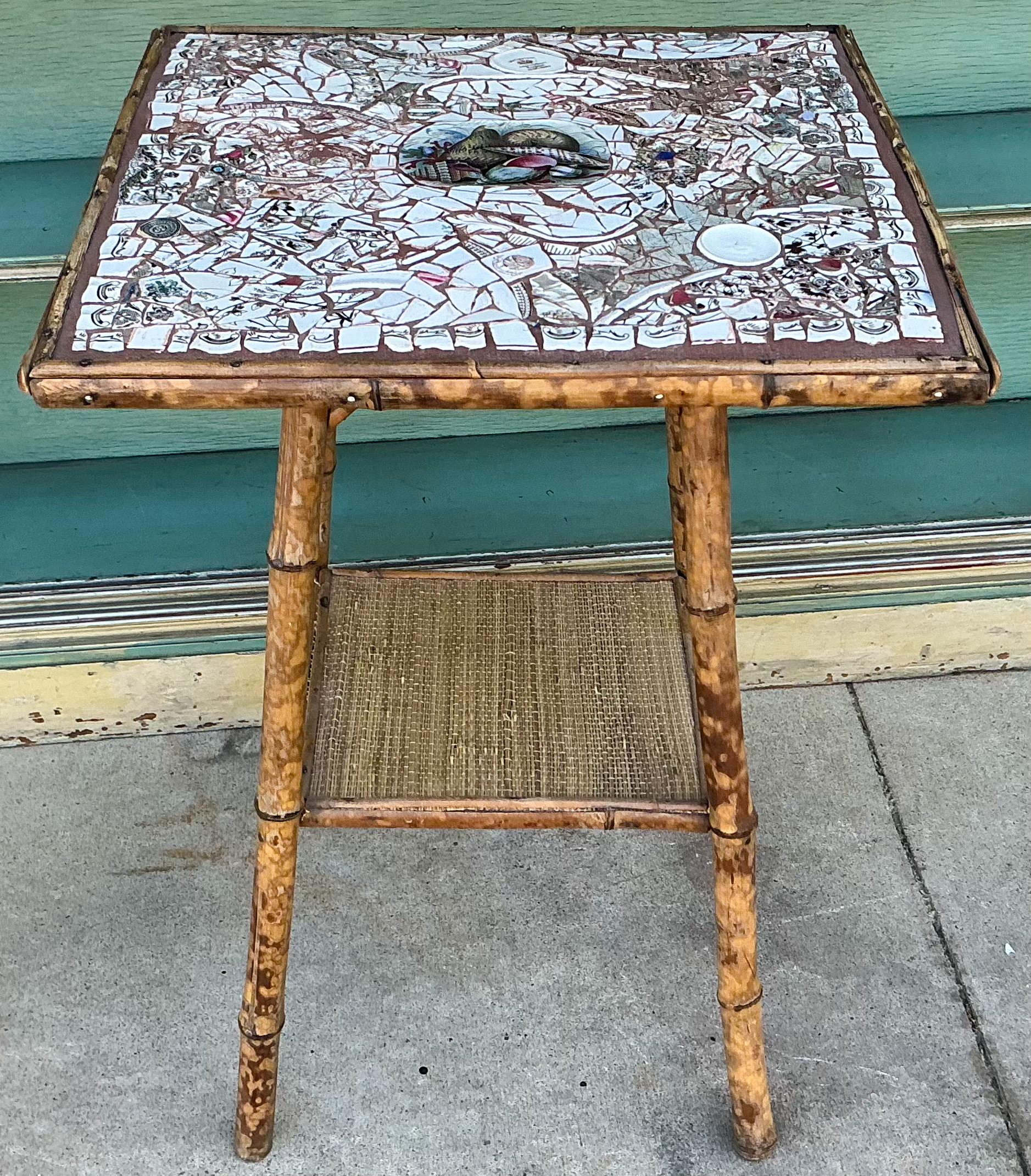 This is an English burnt bamboo side table with a mosaic top comprised of 19th century transwferware. It has a shell motif. The second shelf is grasscloth. It is in very good antique condition.