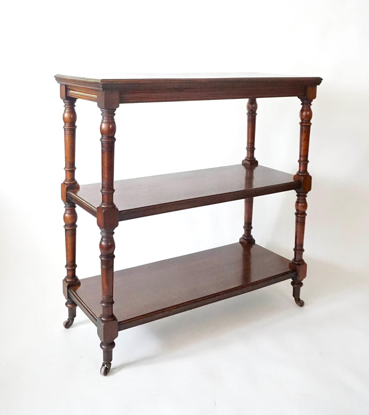 Circa 1880 English solid chestnut etagere attributed to Jas. Shoolbred & Co. of London of rectangular double-sided three tier form having Aesthetic Movement style turned stiles supporting solid plank molded edge shelves and original brass and brown