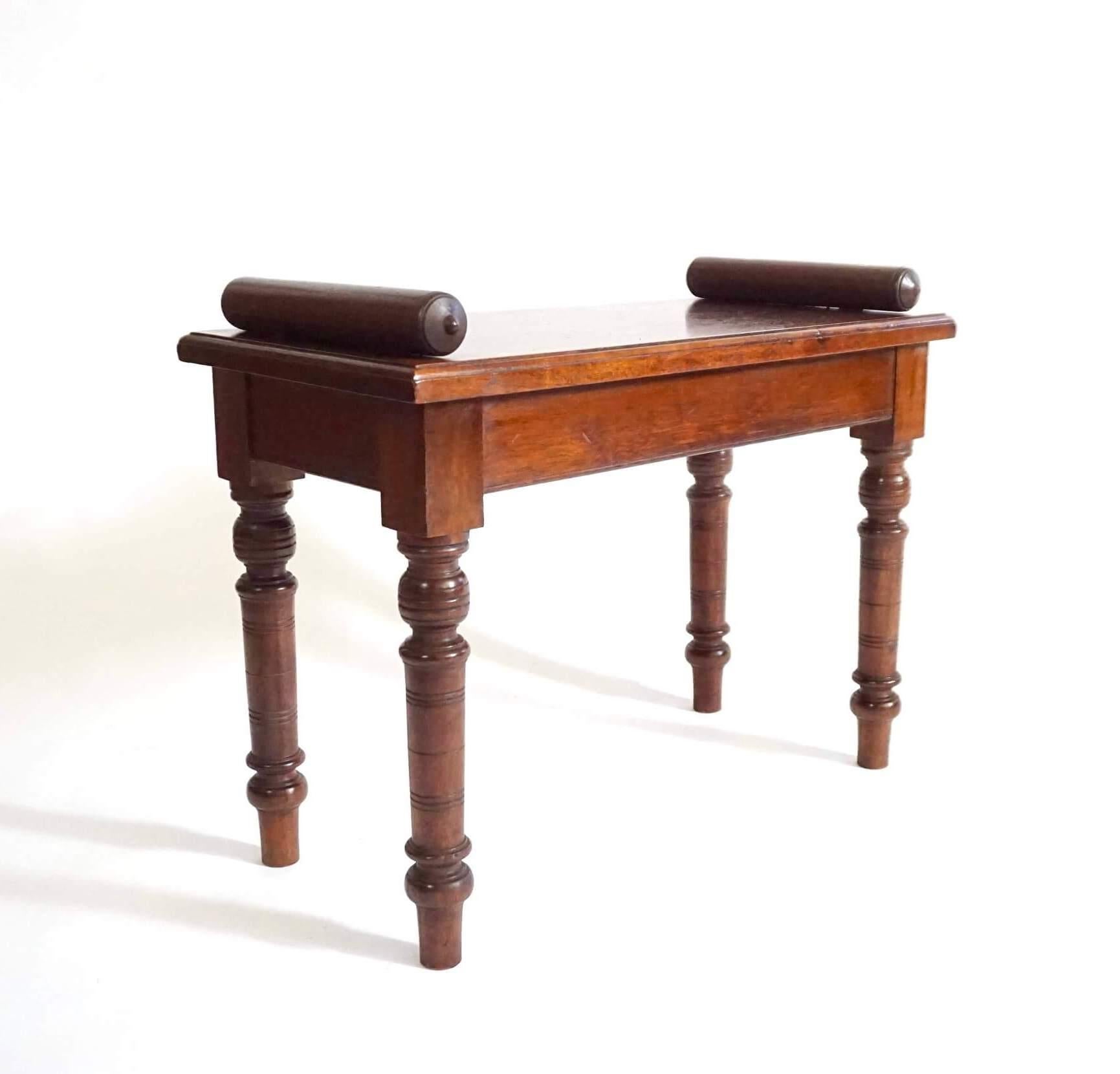 Panca da ingresso o da finestra in castagno massiccio del movimento estetico inglese del 1880 circa, di rara forma a sedile singolo, attribuita a James Shoolbred & Co. di Londra. Il piano rettangolare con bordi modanati è dotato di bolsters