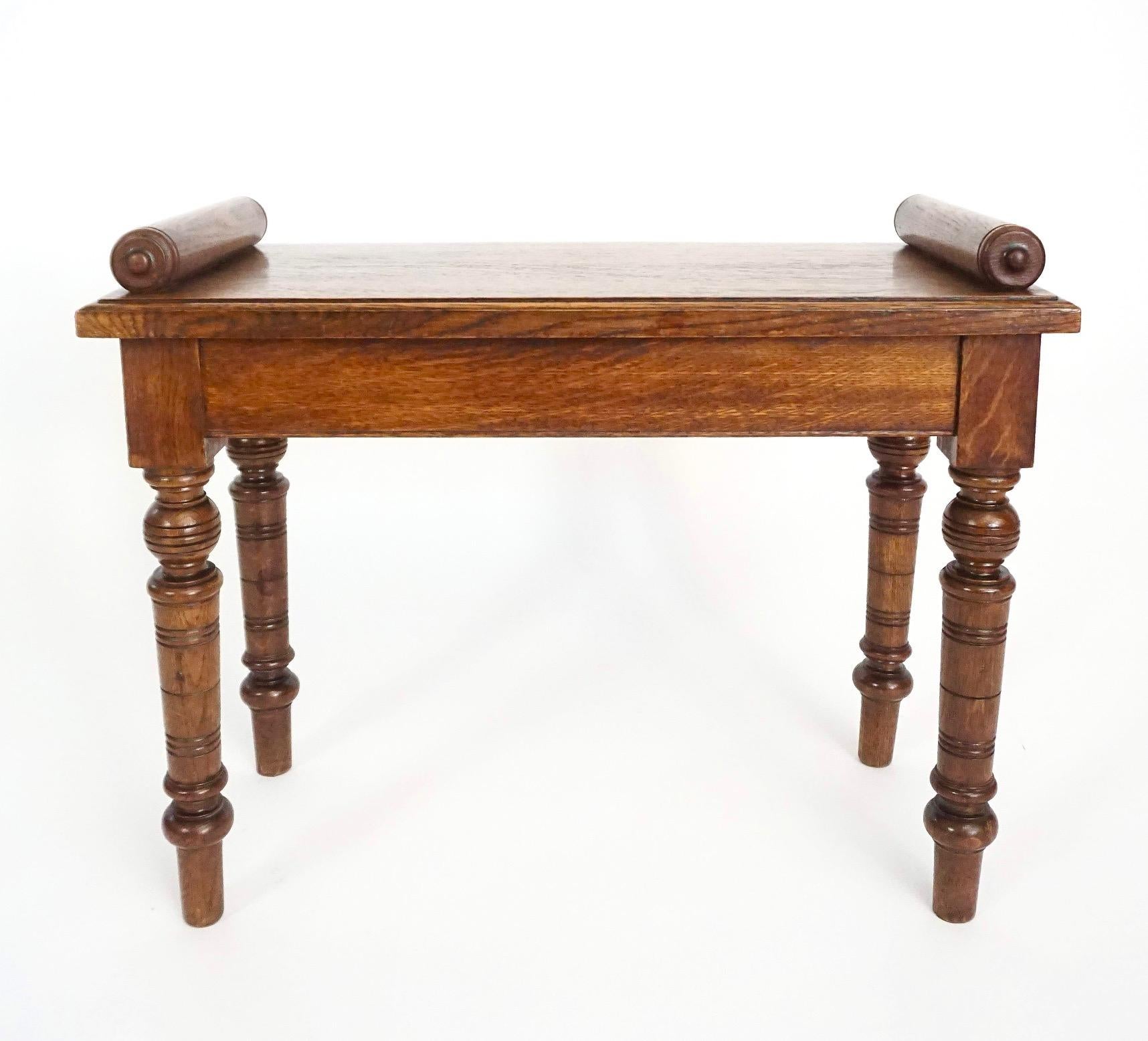 A circa 1880 English aesthetic movement solid oak hall bench or window seat of rare single seat form attributed to James Shoolbred & Co. of London, the rectangular molded-edge top with turned cylindrical bolsters each end above flat friezes joining