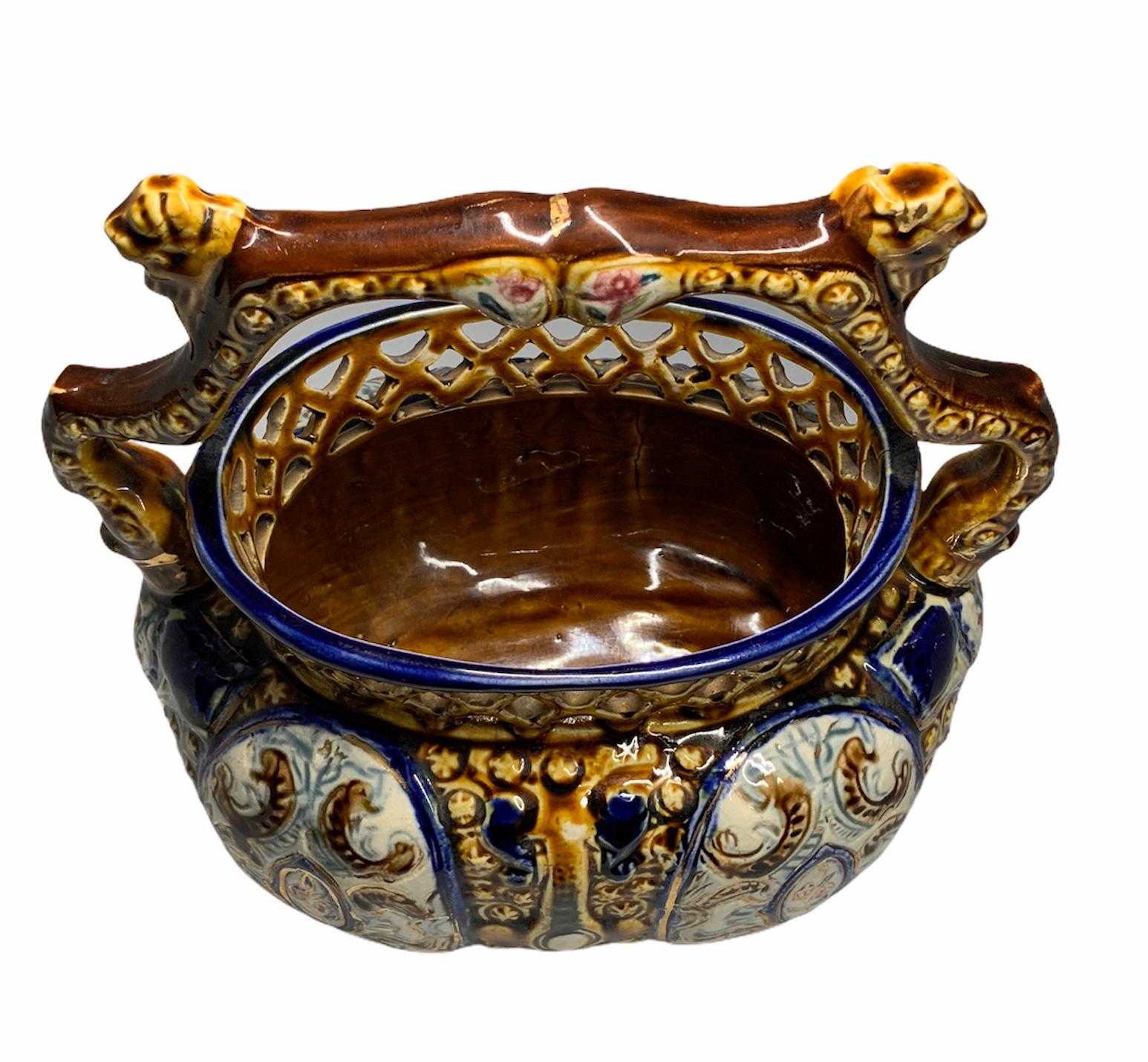 This is an English Majolica oval bulbous shaped basket. It is hand painted with bright cobalt blue, brown and white. It is decorated with C- shaped scrolls and some cameo of roses. The upper border is adorned with a pierced diamonds net. A brown