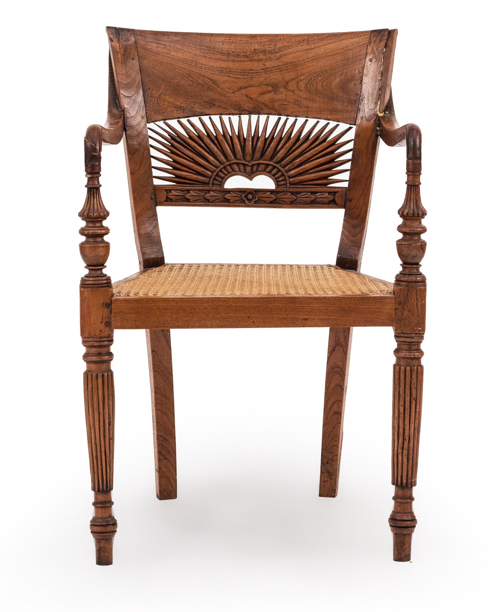 English Anglo-Indian teak arm chair with a cane seat and a slat sunburst carved back with fluted legs. (repair to back)