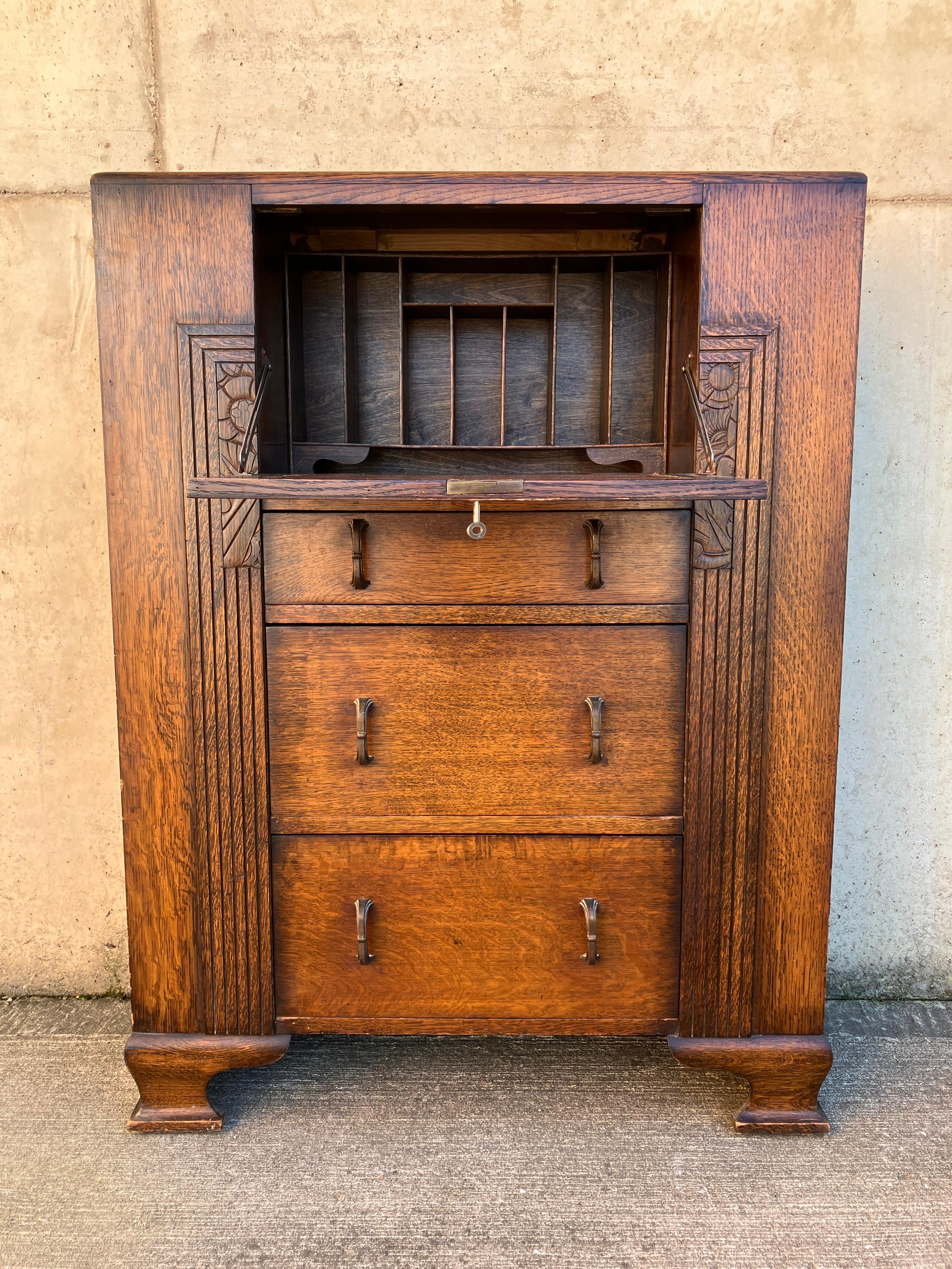 Magnifique bureau ancien anglais des années 1920. Ce meuble compact de style Art déco abrite une table d'écriture et des trous de pigeon pour les petits objets derrière une porte rabattable. Trois tiroirs avec de jolies poignées en métal. Sur les