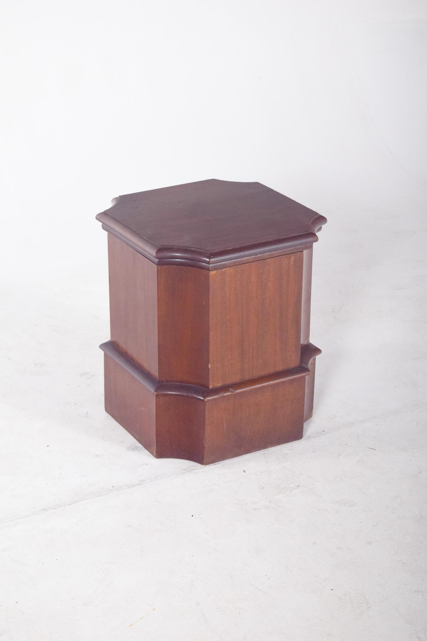 Armoire à pots de chambre octogonale en acajou. Avec son plateau découpé et son cadre biseauté, il révèle un travail de menuiserie soigné. L'intérieur abrite un récipient blanc, inséré dans la rainure circulaire du plateau, ce qui permet de