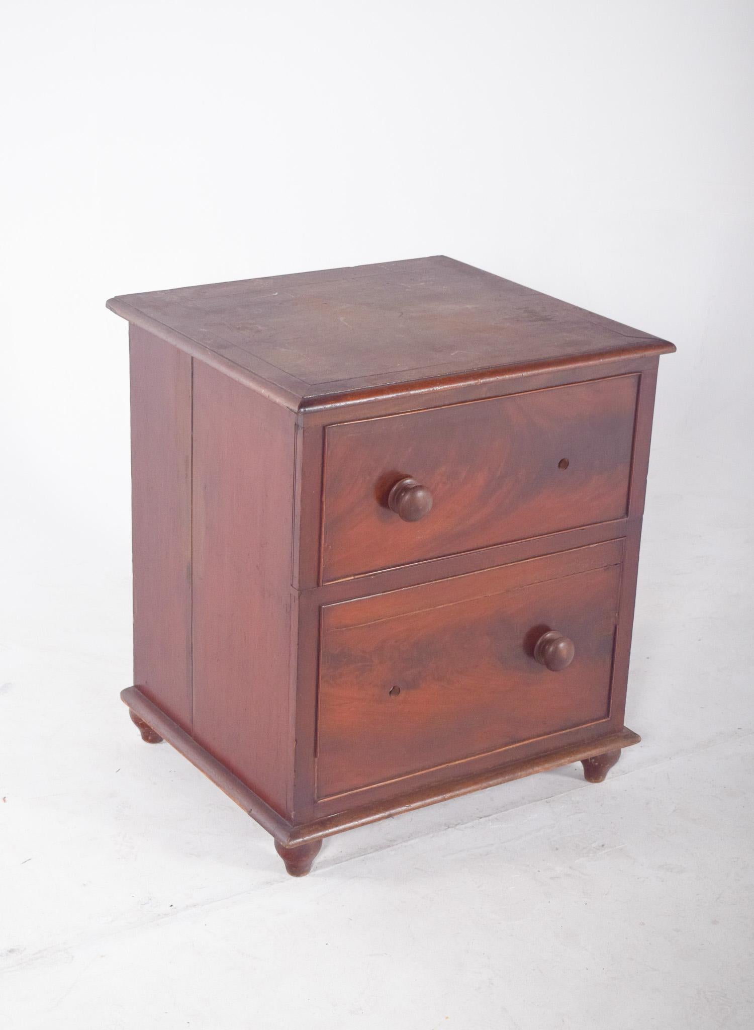 Commode ancienne avec un design qui simule une petite commode, ce meuble a une structure robuste et une finition vernie rougeâtre. Le couvercle supérieur se soulève à l'aide de charnières, révélant un siège à ouverture circulaire, utilisé à
