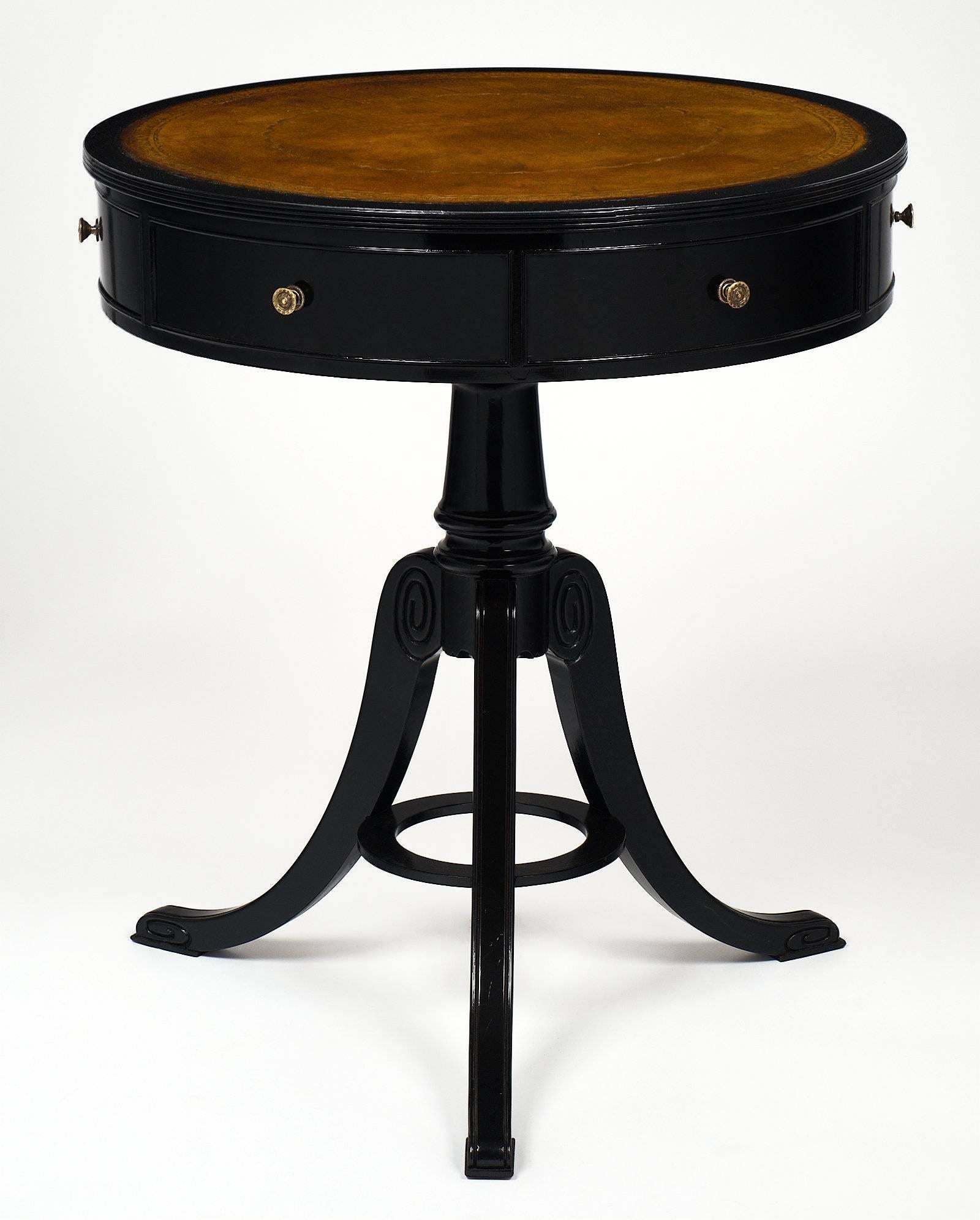 English Victorian style “gueridon” with gilt embossed leather top. The table has two drawers and four faux drawers. There is a circular stretcher between the three curved legs. The table is made of mahogany that has been ebonized and finished with a