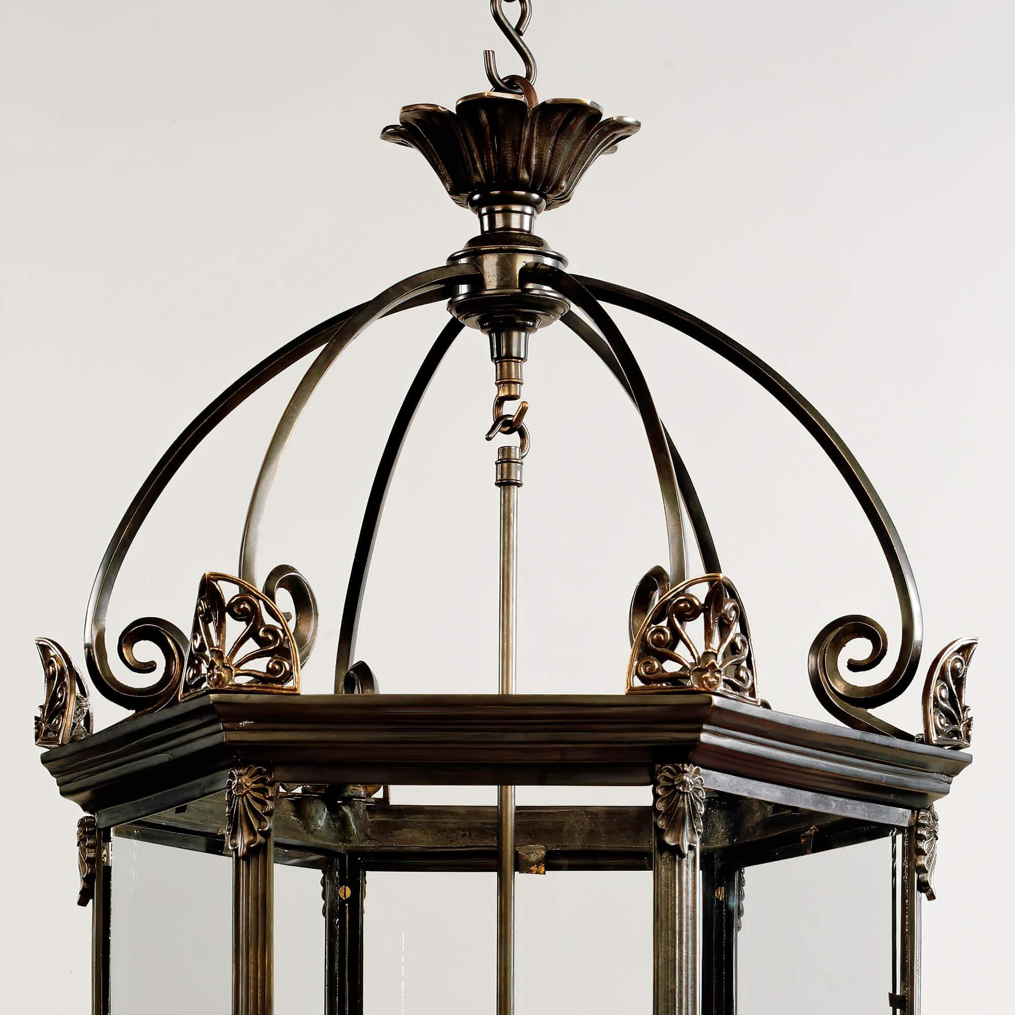 A fine large scale English antique style hall lantern with brass scrolling crown, with anthemion form mounts to the hexagonal frame, with a stepped molded edge, with a stop fluted frame and door and having additional ornamental anthemion mounts and