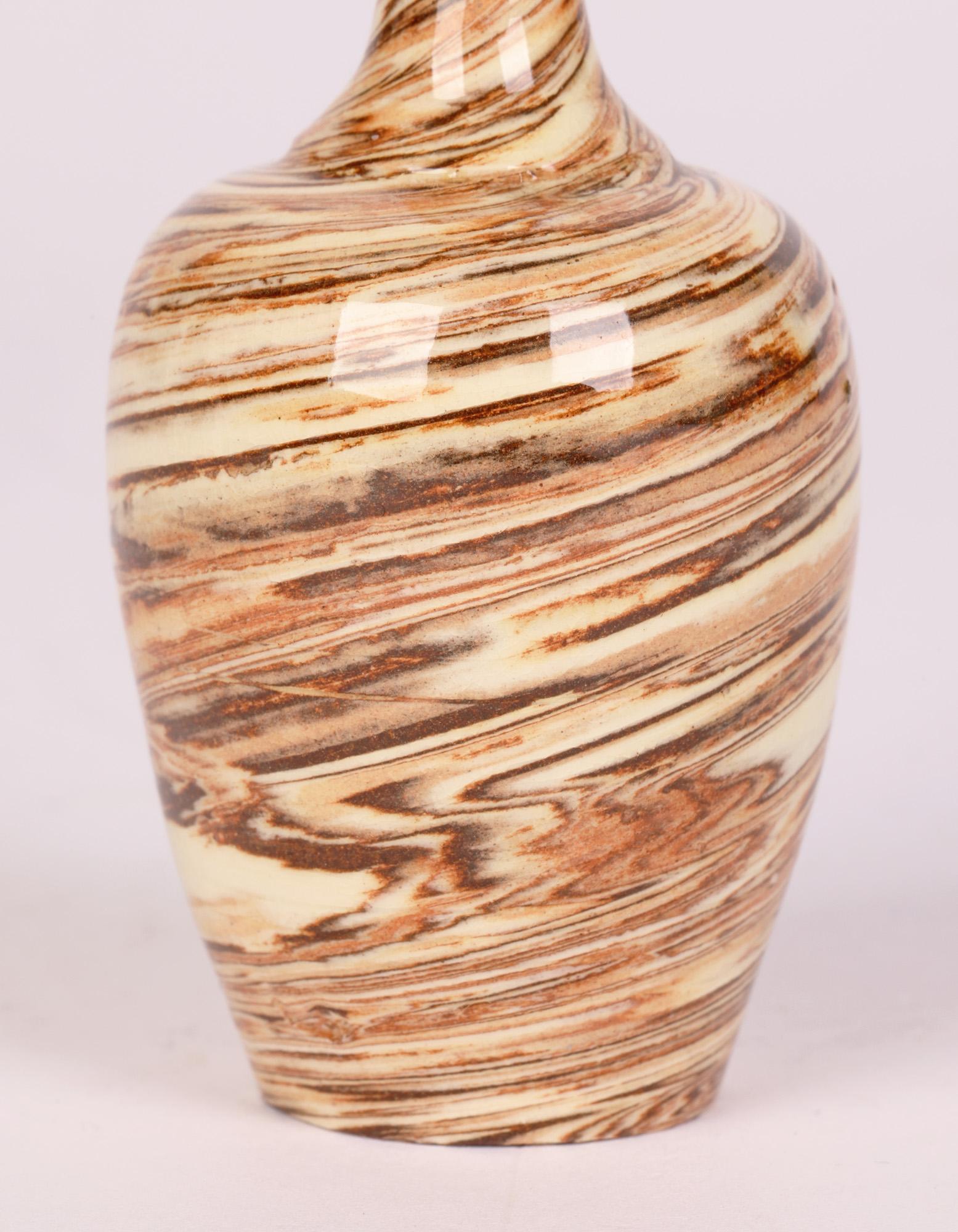 A stunning antique English miniature slip ware agate pattern pottery vase of bottle shape dating from the 19th century. The vase stands on a narrow round foot with recessed base and has a round bulbous shaped body and tall slender neck widening