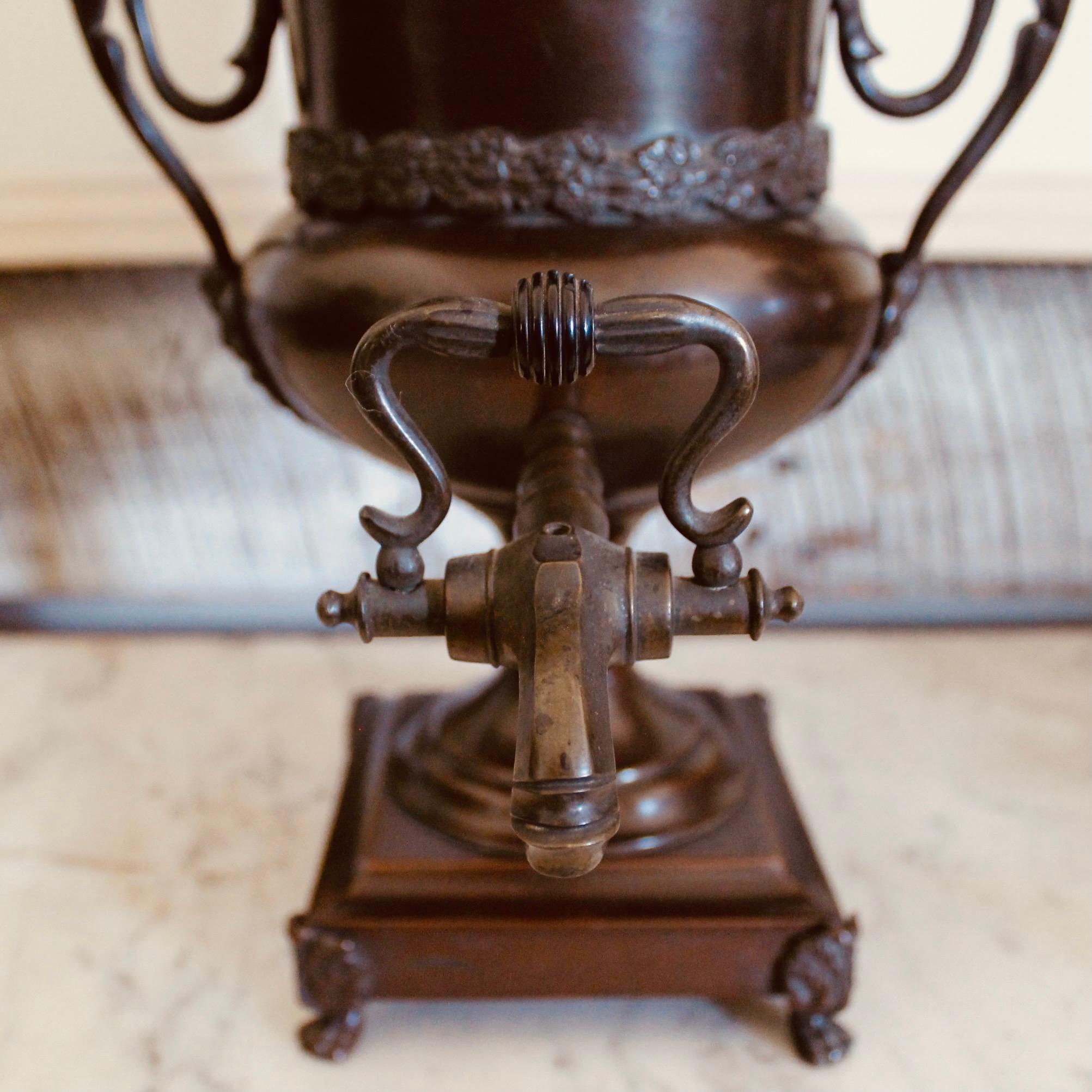 A very fine and decorative ca. 1810 footed hot water urn of dark patinated copper, with wonderful sculptural details in the manner of Wedgwood ceramics of the same period. A golden putto serves as the handle for the two part lid... a small opening