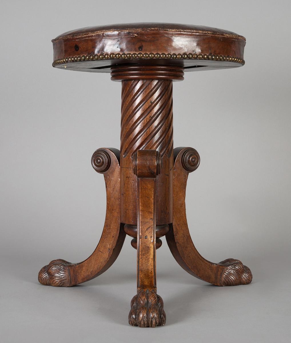 Regency mahogany adjustable revolving piano stool on tripod base with spiral carved pedestal terminating in carved finial, the C-scroll tripod legs ending in carved paw feet with the seat covered in the original morocco leather with brass nail heads.