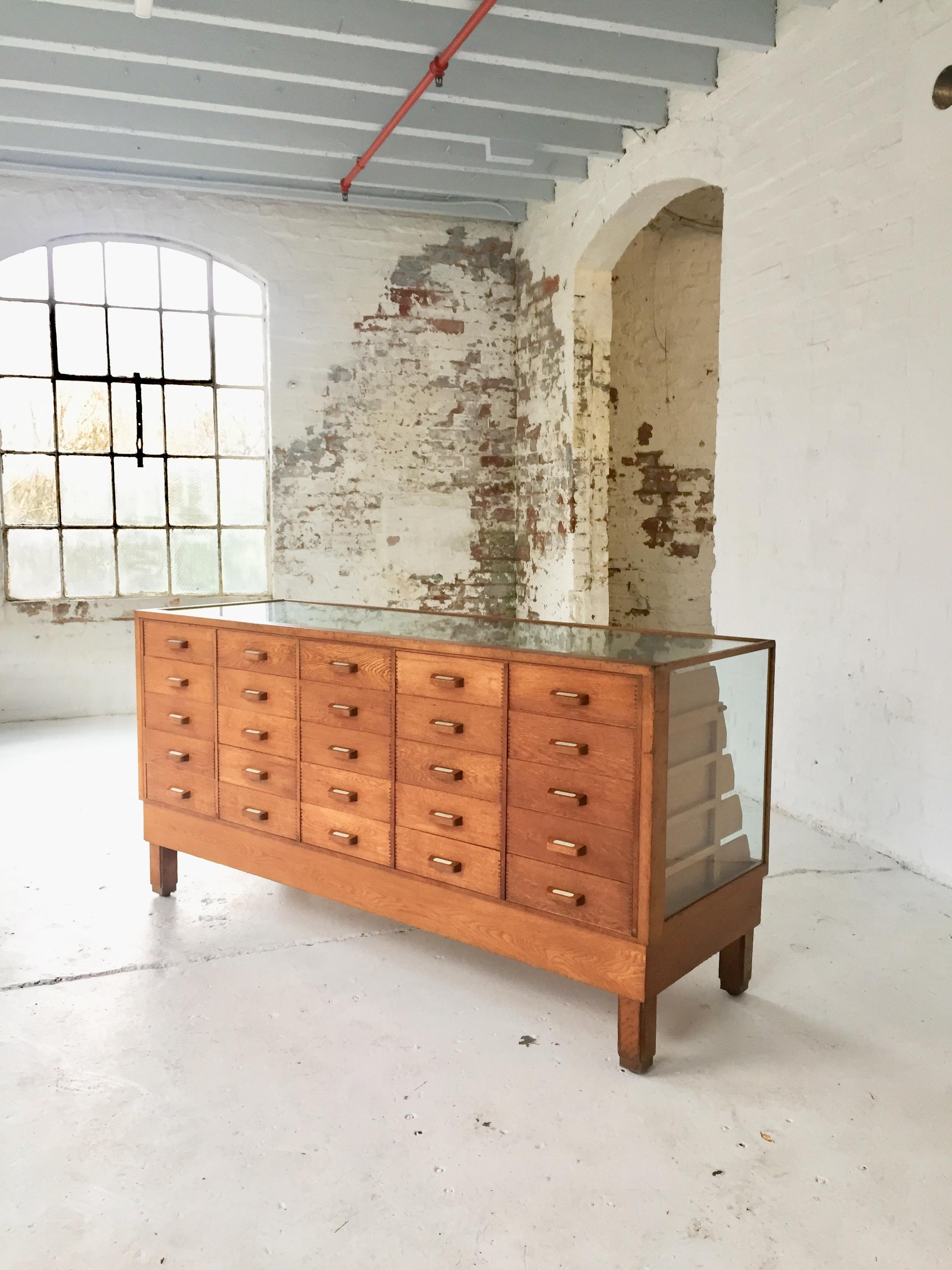 This is an original 1950s shop haberdashery counter made in Birmingham England by Harris and Sheldon Ltd. The large oak haberdashery counter has glass top, sides and front with oak beading around the edges. There are five banks of drawers with five