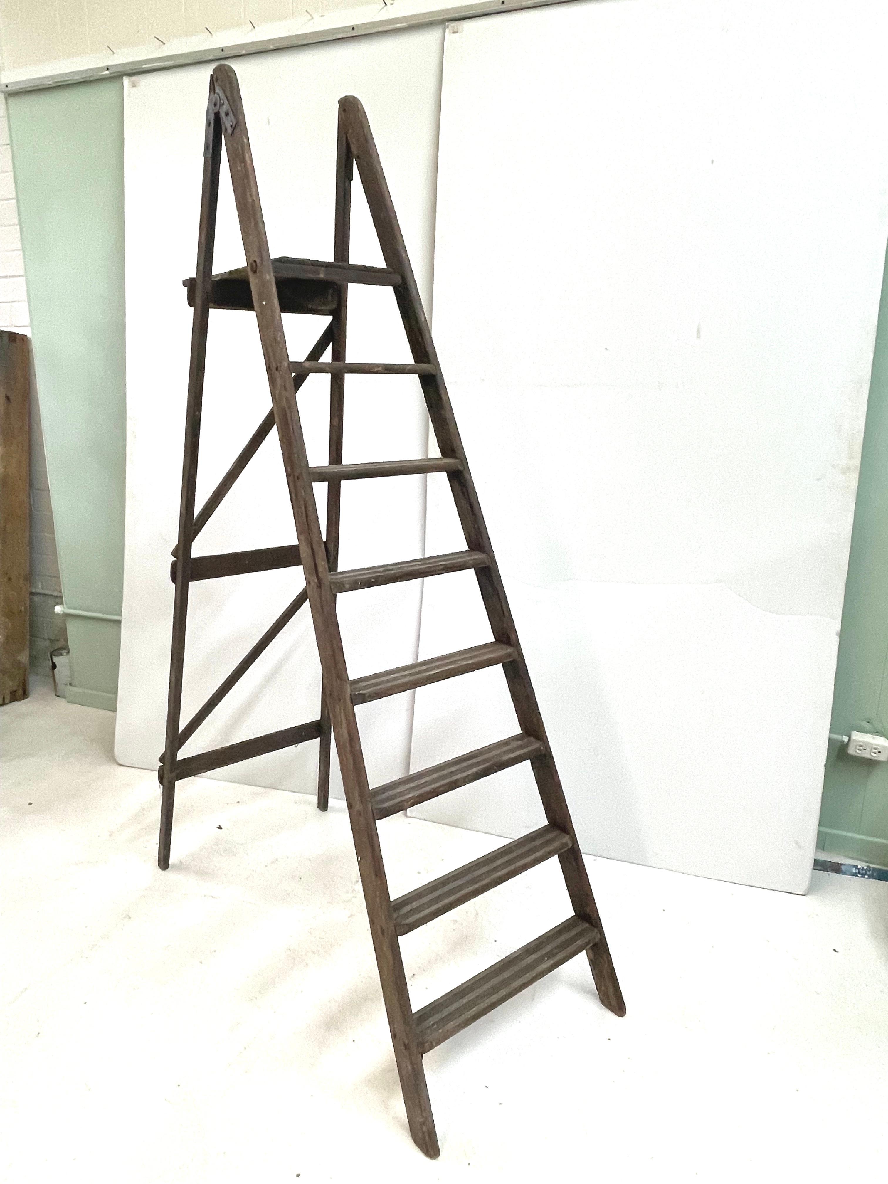 This well-worn and tall late 19th century English seven step folding ladder features a tray shelf at the top and has the original brackets, hardware, and dowels. The weathered patina of the wood has beautifully faded to a warm silver tone. The