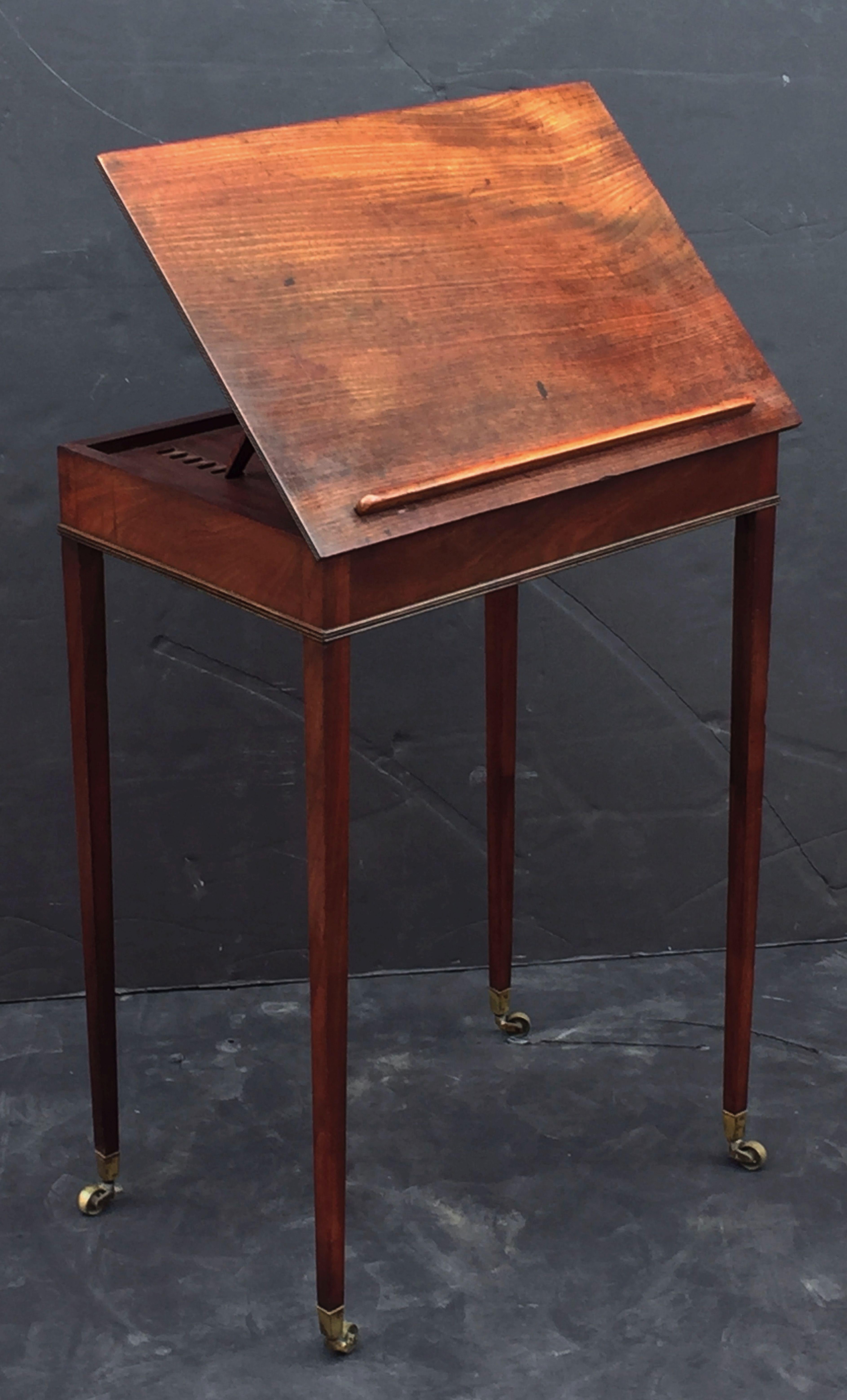 A fine English architect's drawing table of mahogany from the Georgian Era, featuring a moulded slope top with adjustable height stand and brass locking hardware on back, mounted to a cabinet desk frieze with one fitted side drawer and brass