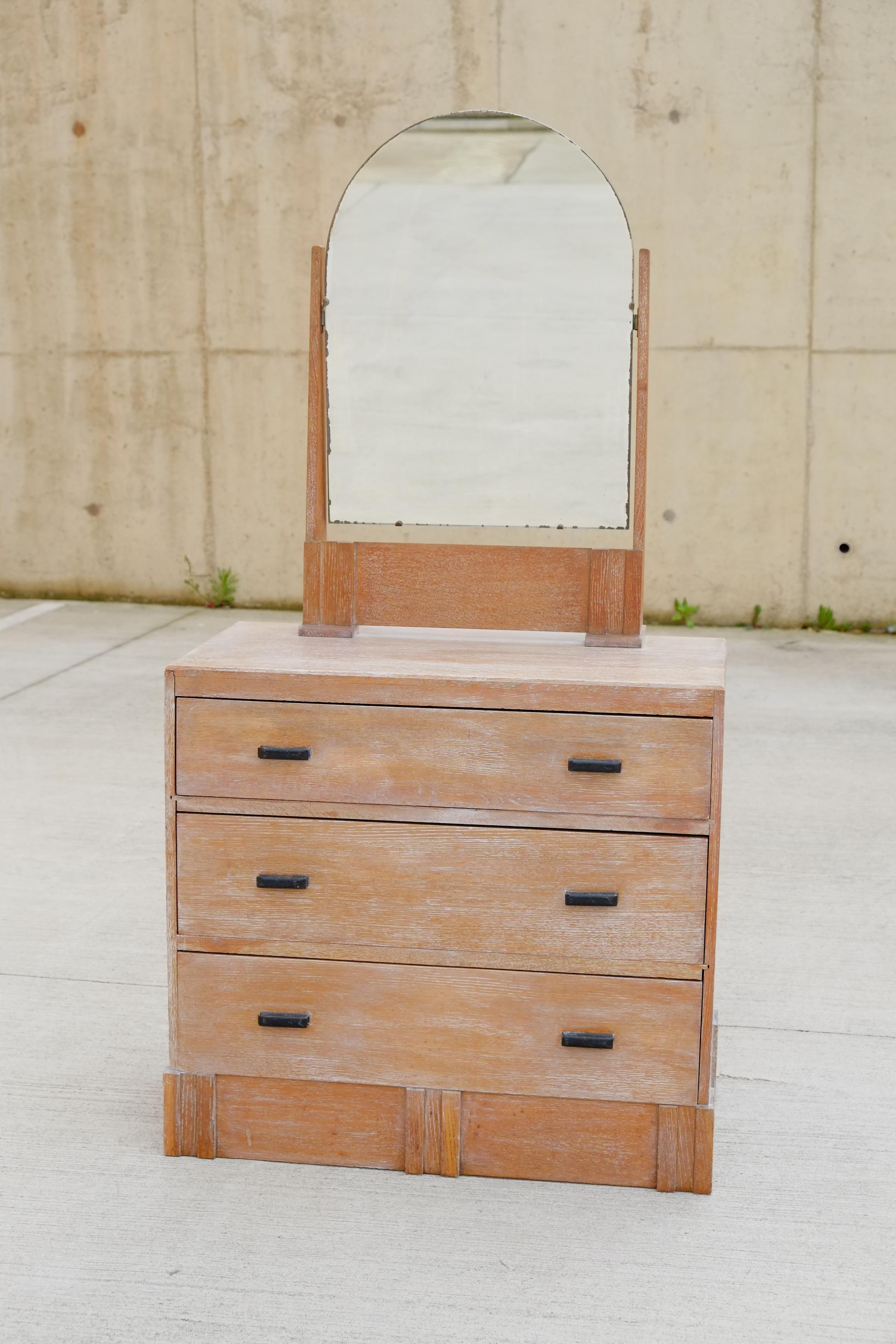 A gorgeous 1930s Art Deco dressing table/vanity from England. Made by Hypnos. This vanity is made of oak with a lime wax finish. Beautiful shape to the mirror. Under the mirror top, there are three large drawers. Lovely black wooden handles to