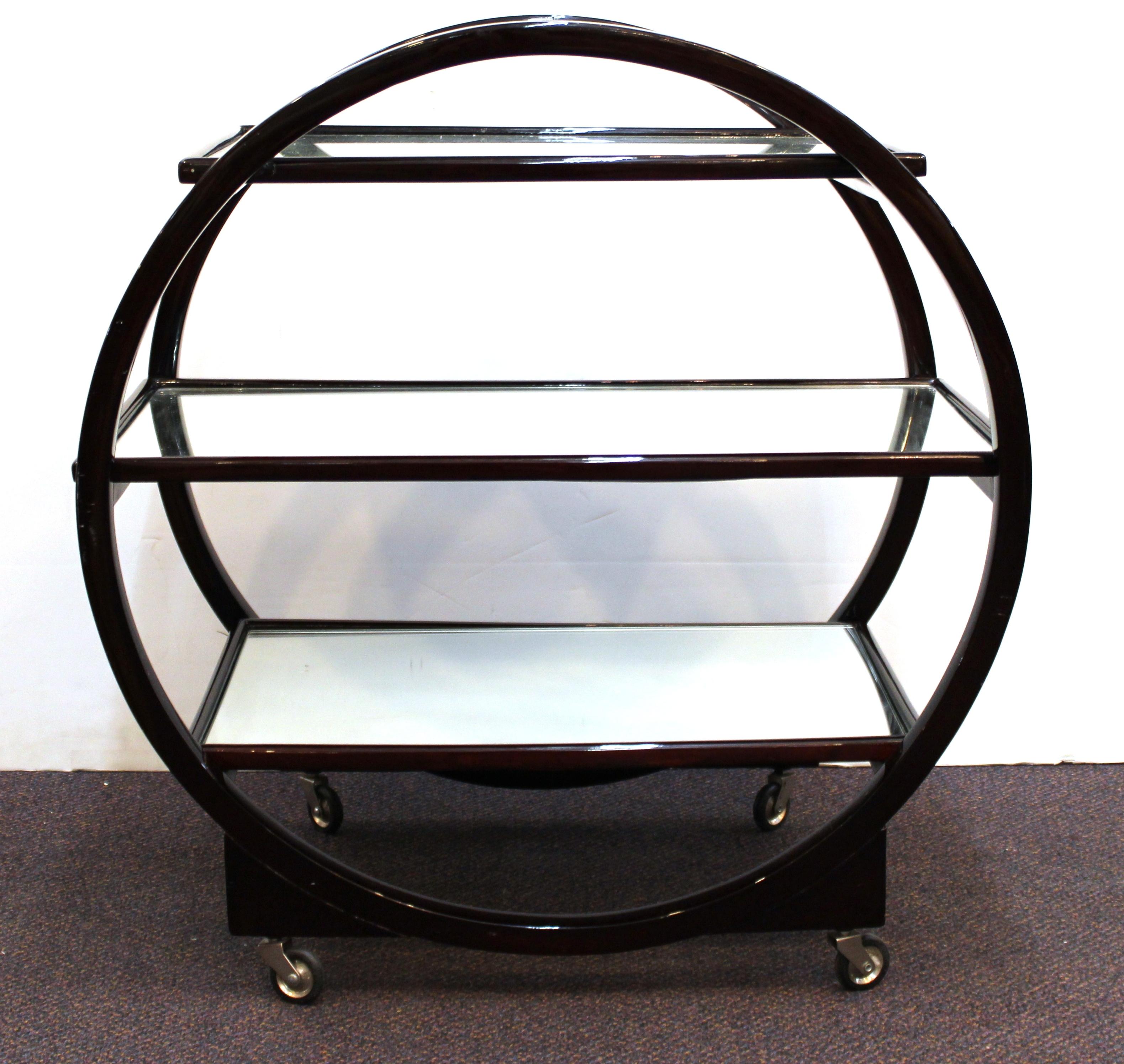 Art Deco bar cart or serving cart with three levels of mirrored shelving set within a circular wooden framework on casters. The piece was made in England during the 1930s and is in great vintage condition, with some age-appropriate wear to the