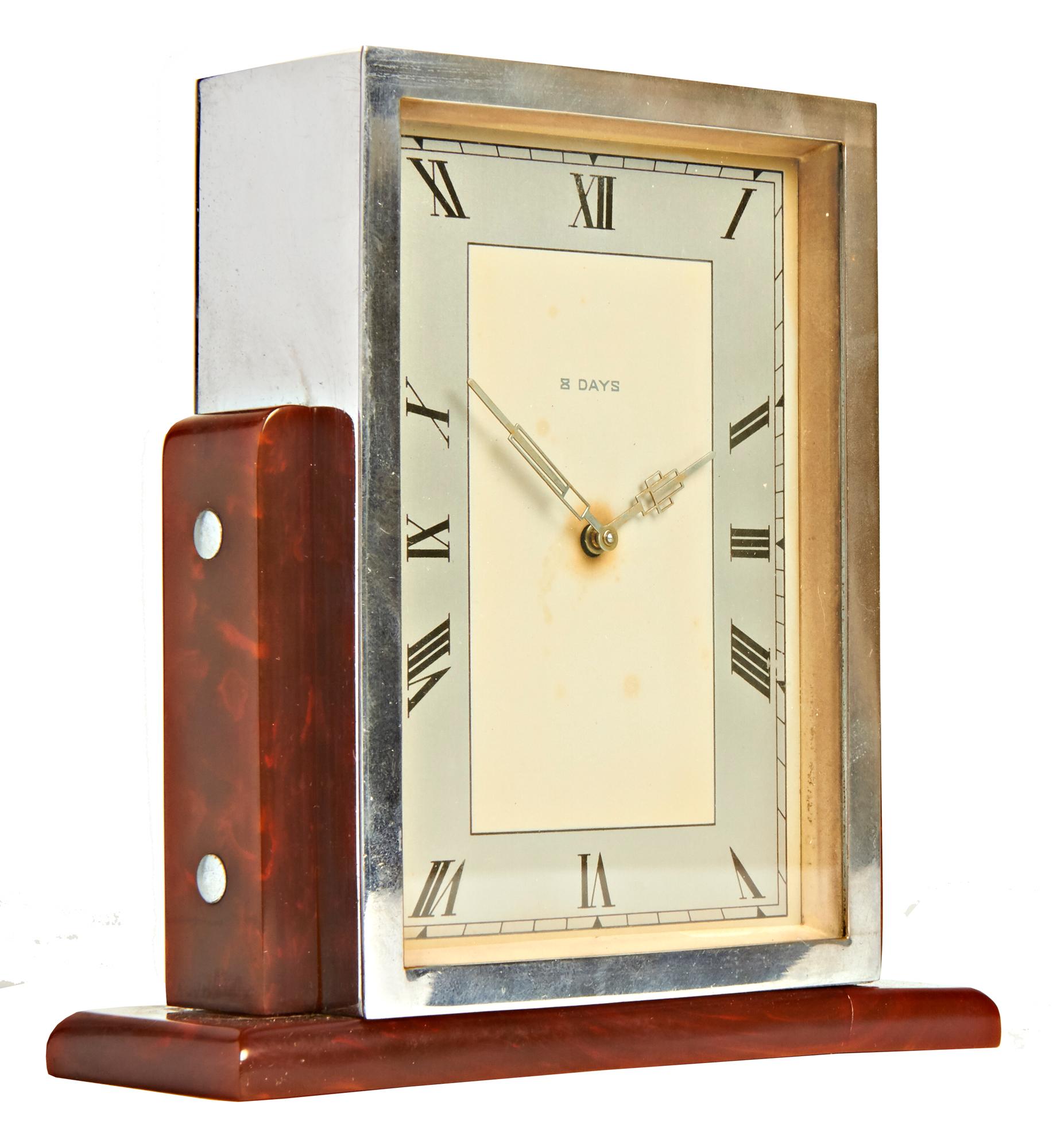 This skyscraper shaped English Art Deco 8-day clock features a totally chrome plated body supported on either side by tortoiseshell/butterscotch Bakelite rounded topped pillars each held in place by by two chrome dome topped bolts and standing on a