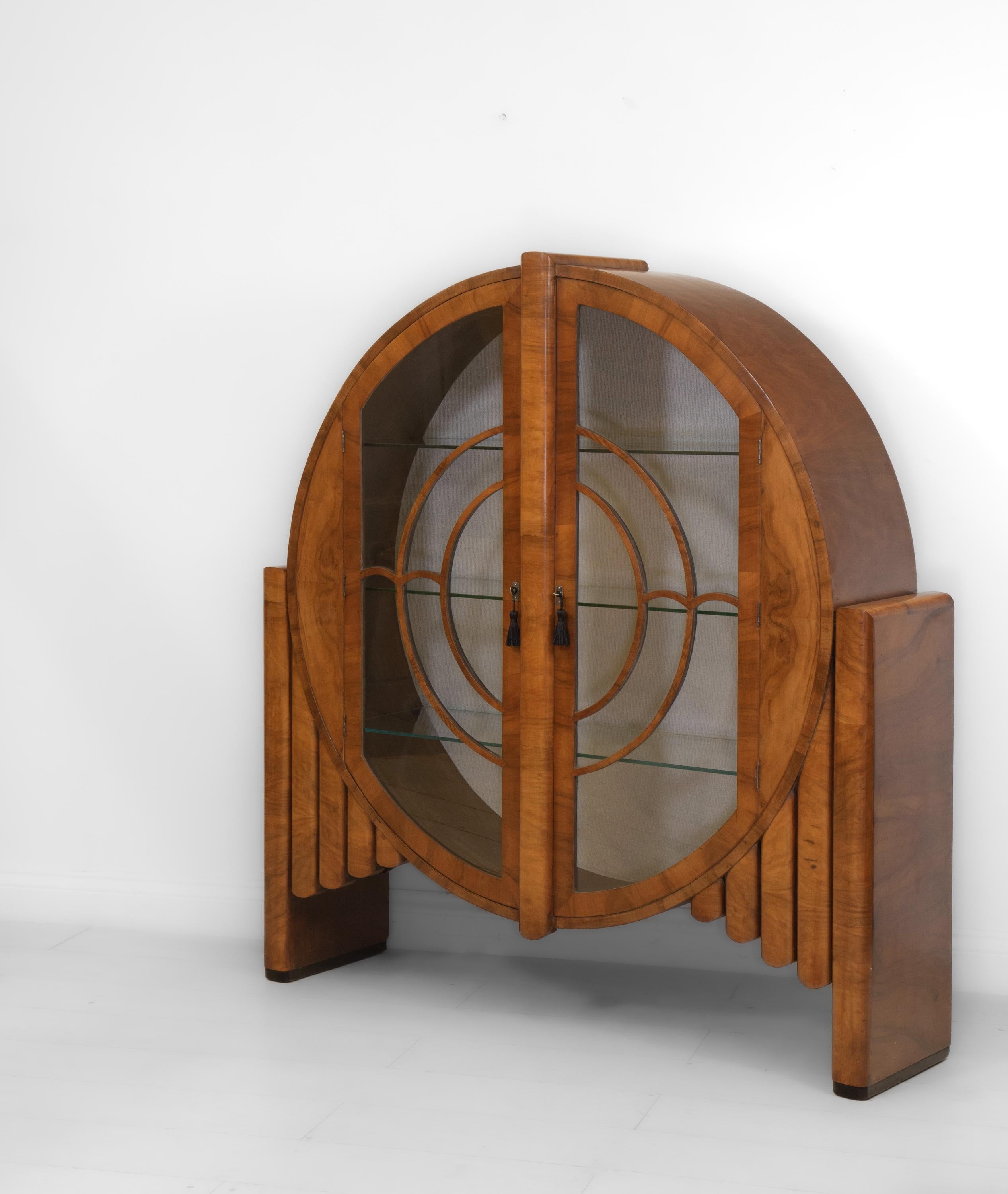 A fabulous English Art Deco circular figured walnut 'Rocket' display cabinet on ebonised plinths. Circa 1930's.

Delivery is INCLUDED in the price for all areas in MAINLAND England & Wales. 

Veneered in highly figured walnut, the cabinet is an