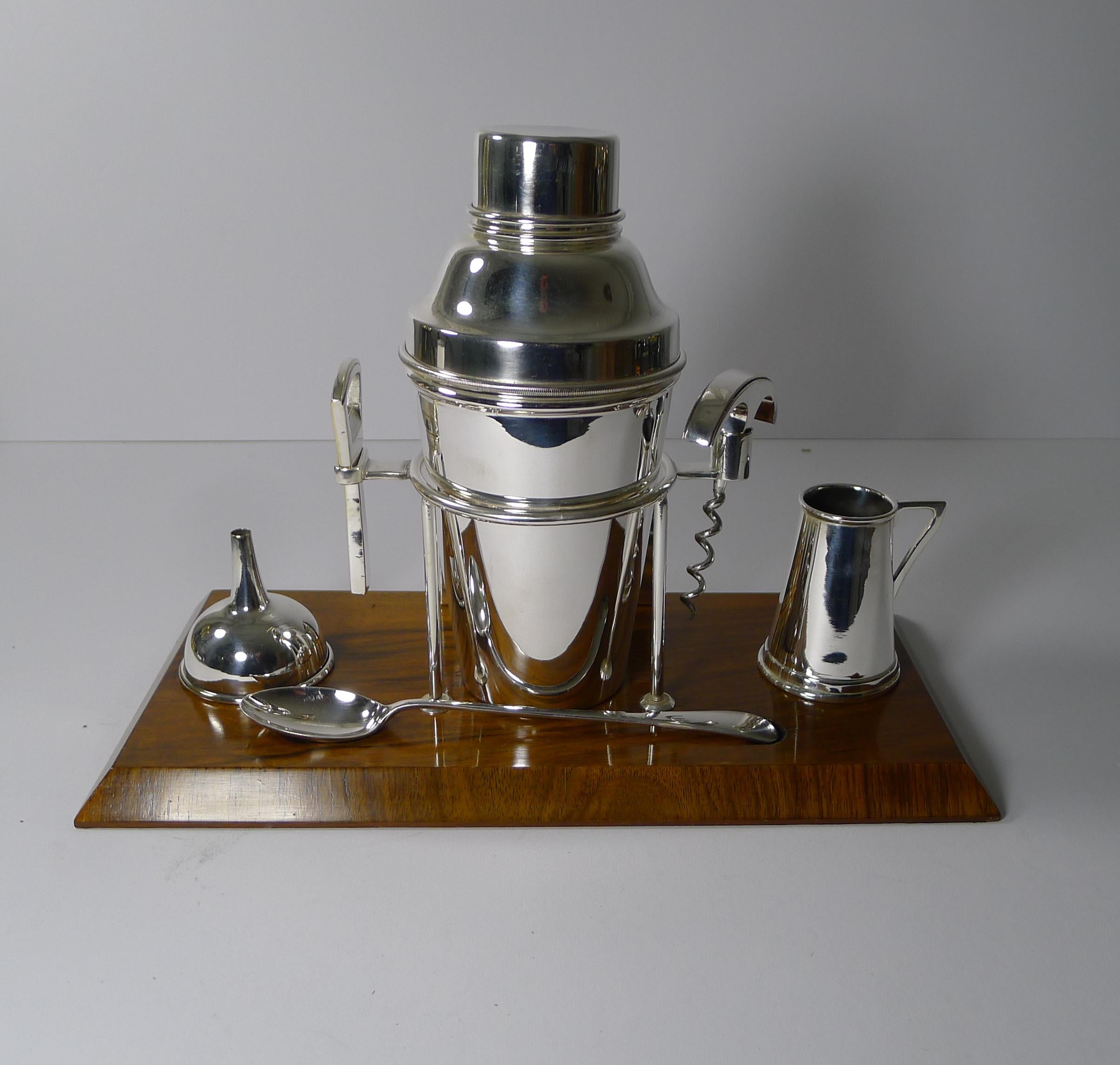 A handsome Walnut and Silver Plated Drinks / Cocktail set dating to c.1930.

The Walnut stand houses a central silver plated cocktail shaker flanked by a bottler opener and corkscrew; to the right is a spirit measure / jigger and to the left is a