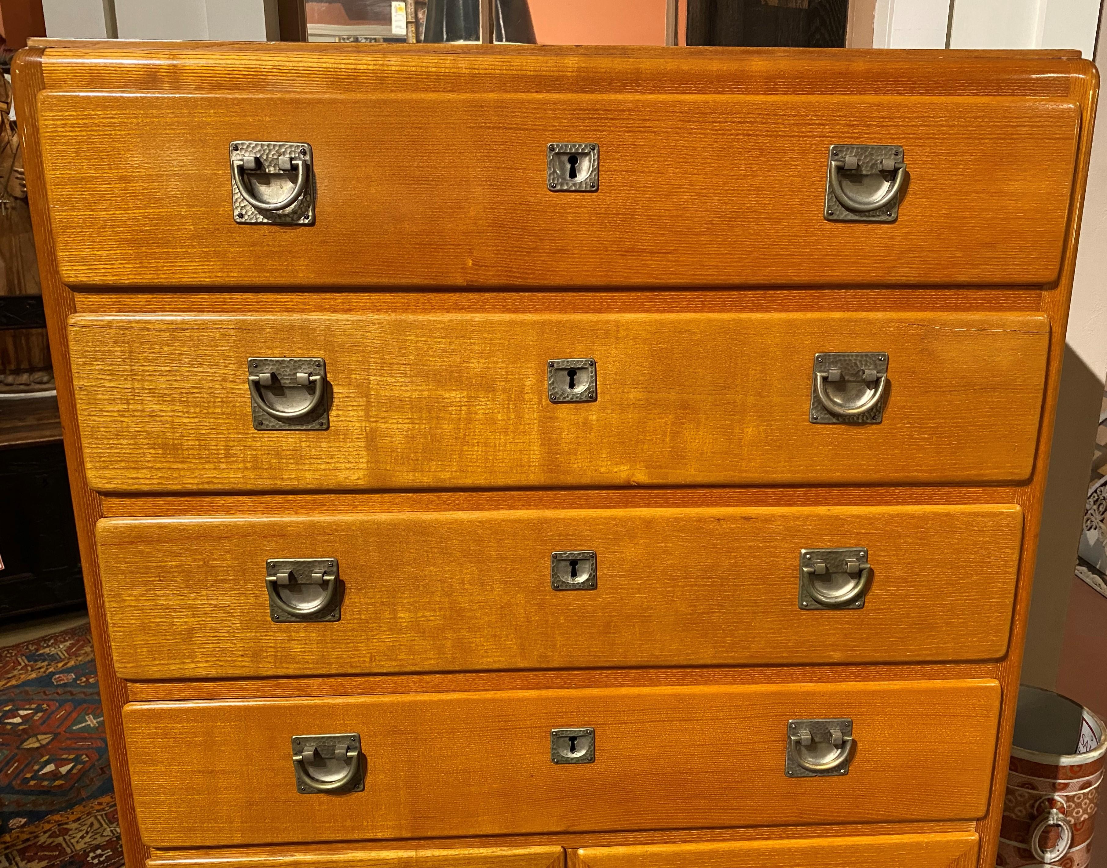 A fine elmwood Art Deco high chest with hand hammered pewter, possibly made by Liberty Furniture, with four upper dovetailed drawers over two blind doors with a variety of  veneers panels, opening to a two shelf storage compartment, paneled sides,