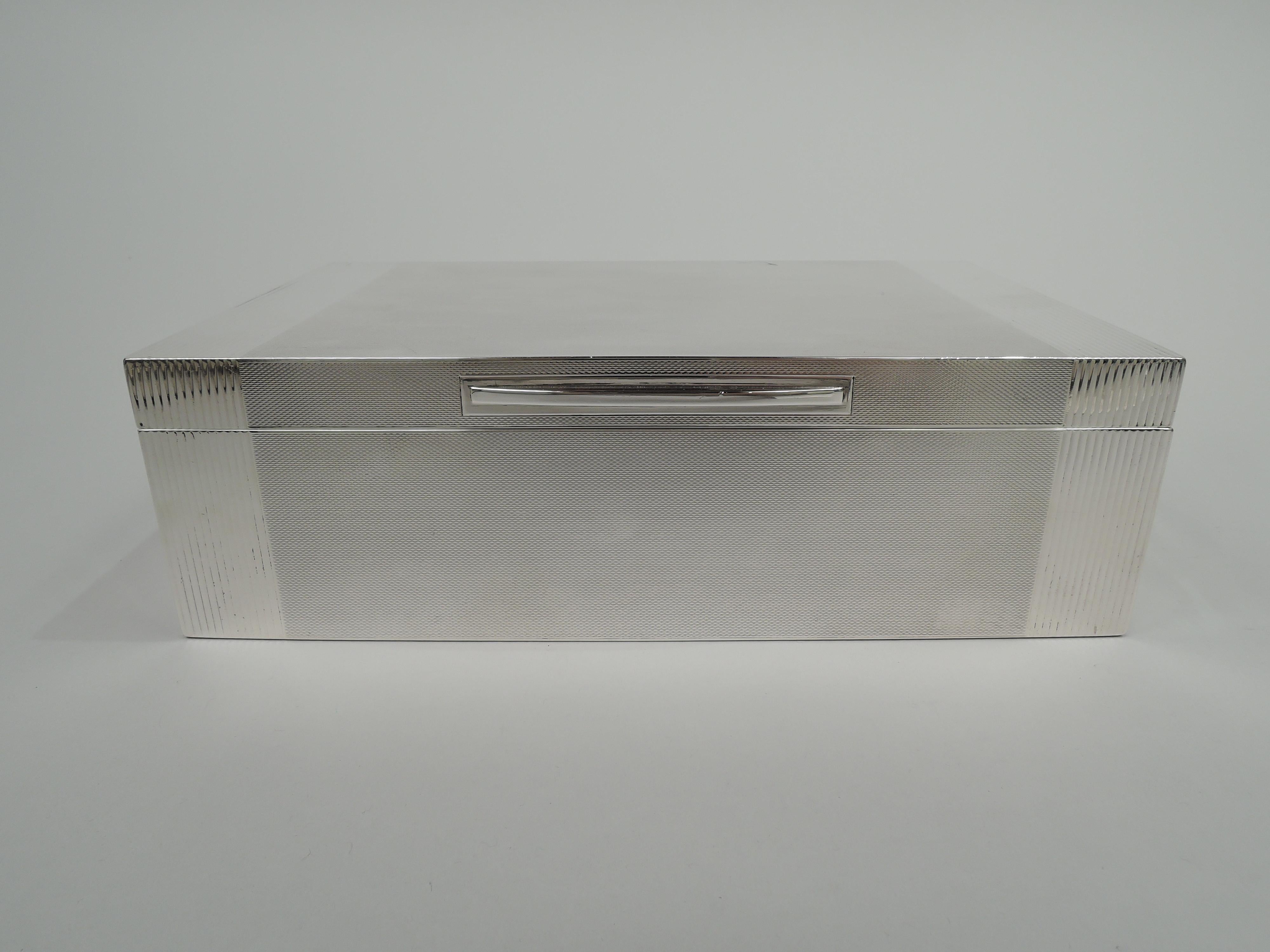 English Art Deco sterling silver box, 1949. Rectangular with straight sides and crisp corner. Cover hinged and flat with tapering tab on plain rectilinear frame. All over engine-turning with reeded bands that wrap around from front to back. Box ends