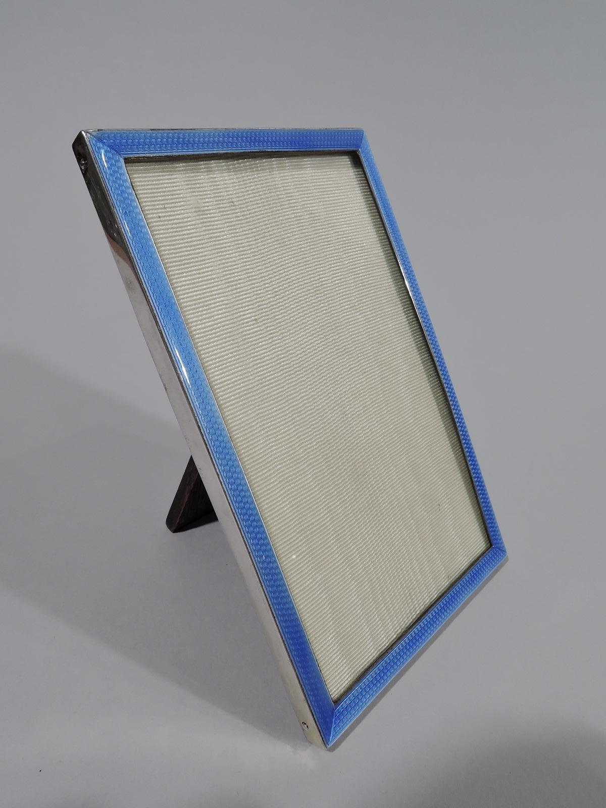 Art Deco sterling silver and enamel picture frame. Made in Birmingham in 1928.Rectangular window bordered by wraparound blue guilloche enamel. Sides sterling silver. With glass, silk lining, and stained-wood back and flush hinged support. For