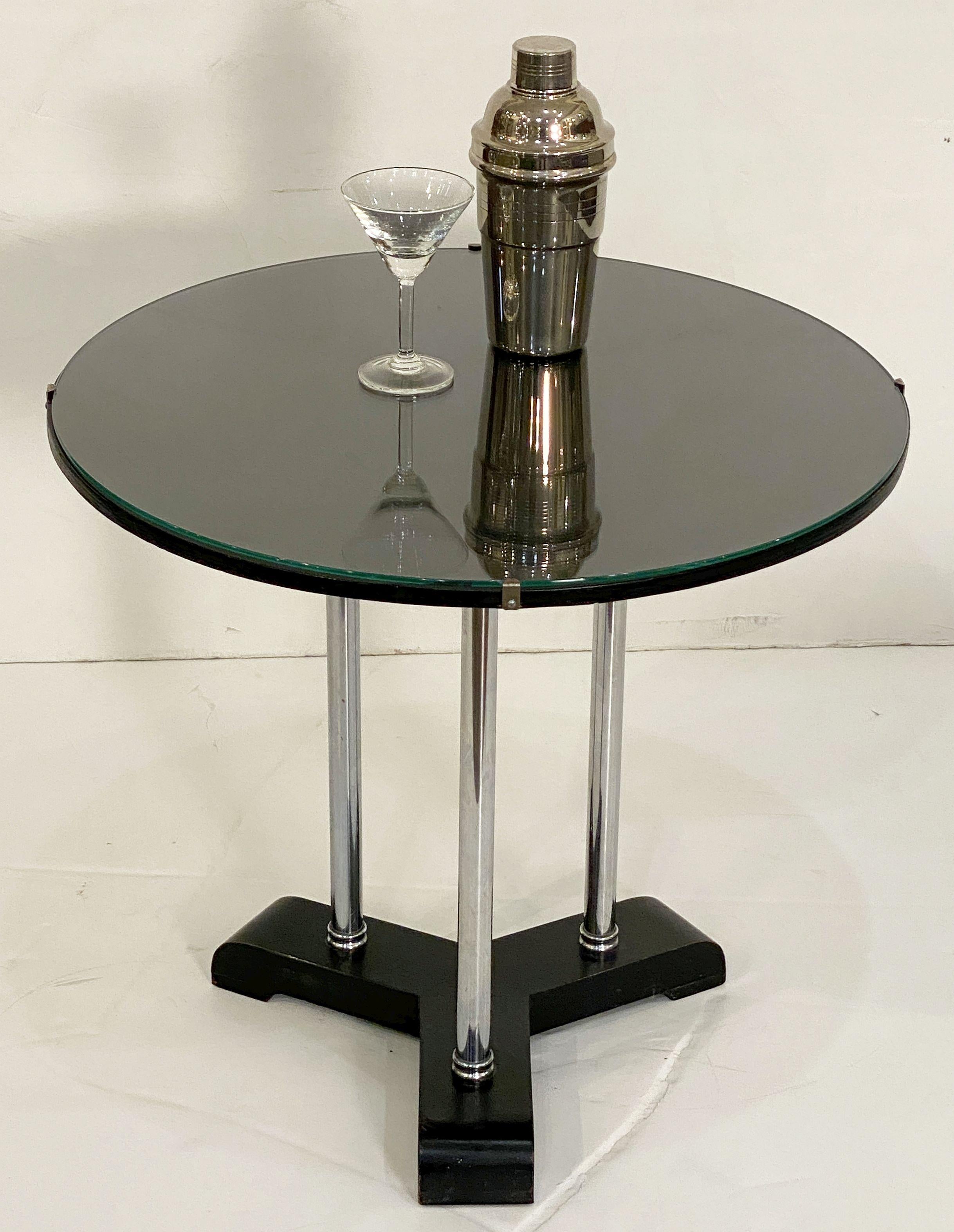 A fine English round or circular side table from the Art Deco era, featuring an upper circle tier of black-painted (ebonized) wood with a glass top, set upon three tubular nickel pedestal column supports, mounted to a bottom tripod base of