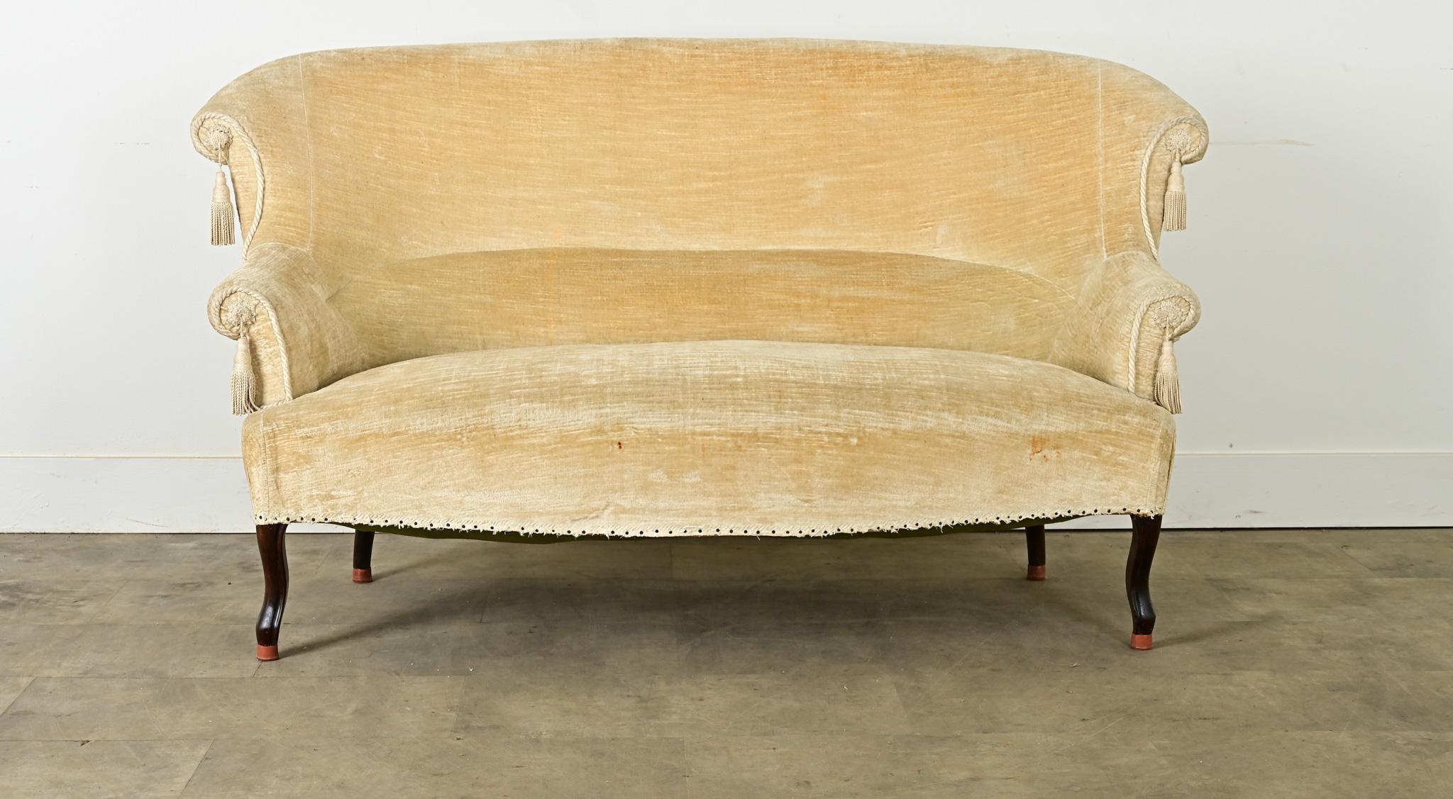 Siting regal and refined, this English settee from circa 1920 is a fantastic size for nearly any room around the home.  The seat back is tall and supportive, plush from the striated velvet upholstery, in a luminous champagne color. Finishing off the