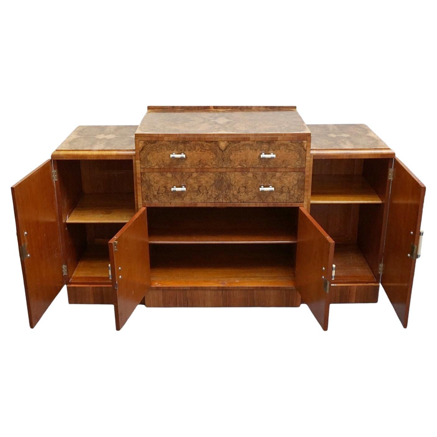 An Art Deco sideboard. Burr walnut veneered with figured walnut banding and original bakelite and metal handles. Two shelved cupboards to either side with central upper drawers and lower cabinet section.

Dimensions: H 95cm - 105.5cm W 183.5cm D