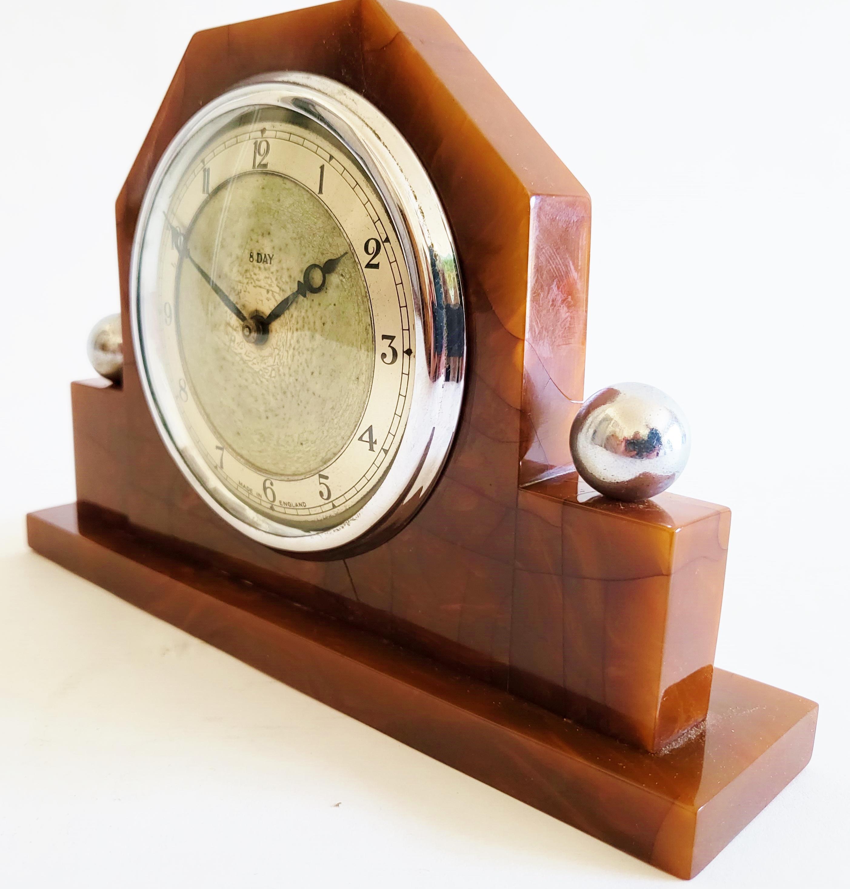 This very pretty English Art Deco 8-day mechanical desk clock features a geometric body of solid tortoiseshell with a bezel in polished chrome. Topping the two Bakelite pillars on either side are two polished chrome spheres and as befitting a