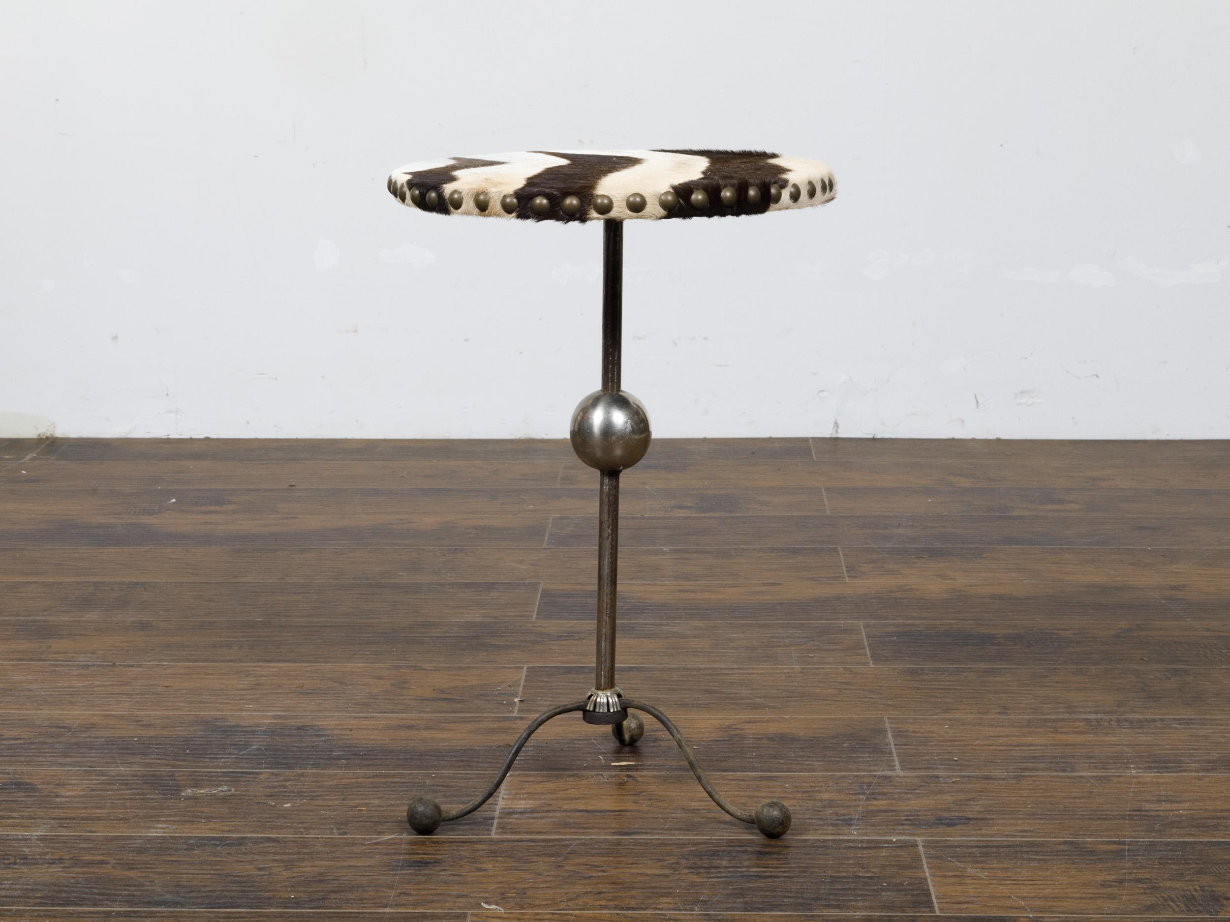 An English Art Deco steel guéridon side table with zebra hide upholstered top, sphere motif and scrolling tripod base. This striking English Art Deco steel guéridon side table, dating back to the Art Deco era, makes a bold statement with its zebra