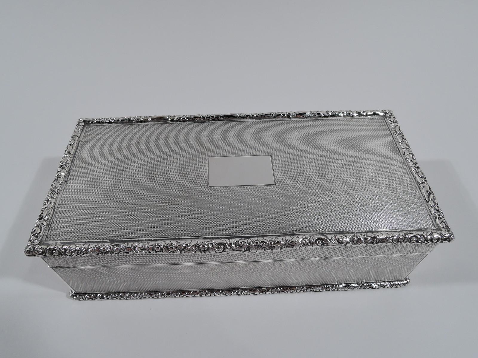 George V sterling silver box. Made by Richard Comyns in London in 1930. Rectangular with hinged cover. Allover engine-turned wave ornament. Rim and base have applied and tooled flower-and-scroll rim. Cover top has plain rectangular frame (vacant).