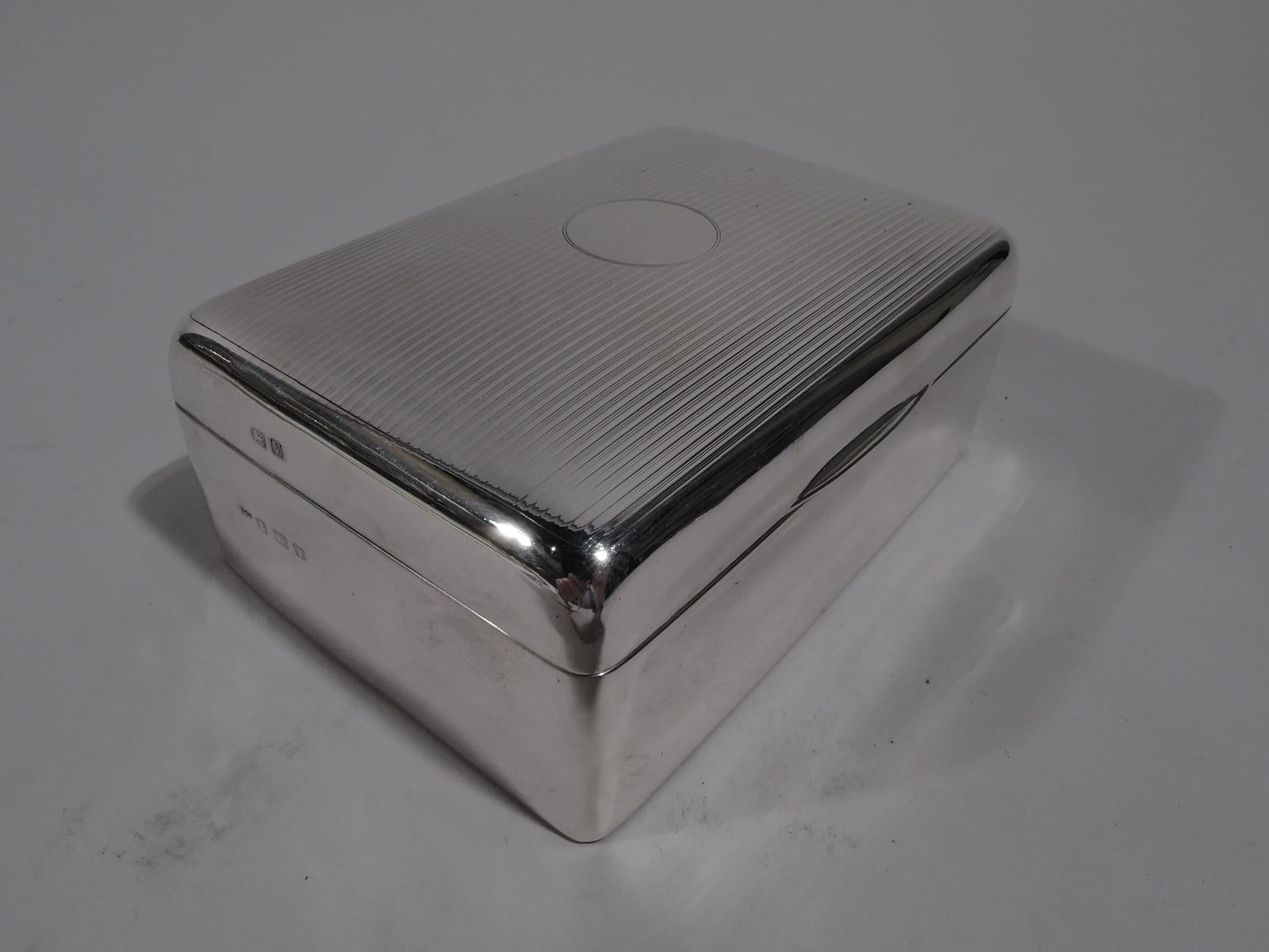 George V sterling silver box. Made by Charles S. Green & Co. in Birmingham in 1920. Rectangular with straight sides and curved corners. Cover hinged, curved, and tabbed. Cover top has engine-turned horizontal lines and central circular frame