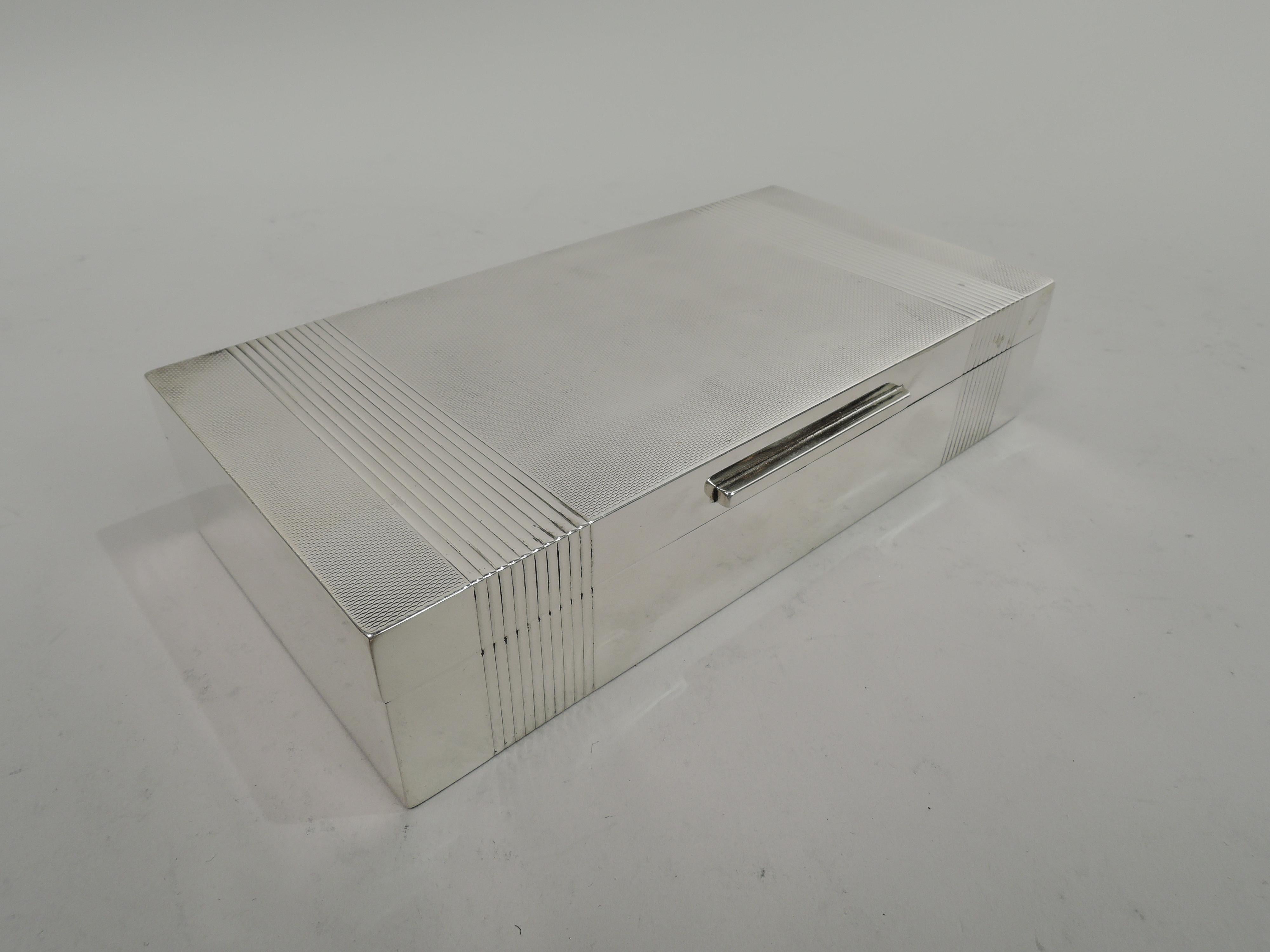 English Art Deco sterling silver box, 1950. Rectangular with straight sides. Cover flat, hinged, and tabbed. Plain sides and engine-turned cover top. Wraparound ribbed bands at ends. Cedar-lined interior. Open felt-lined bottom. Fully marked